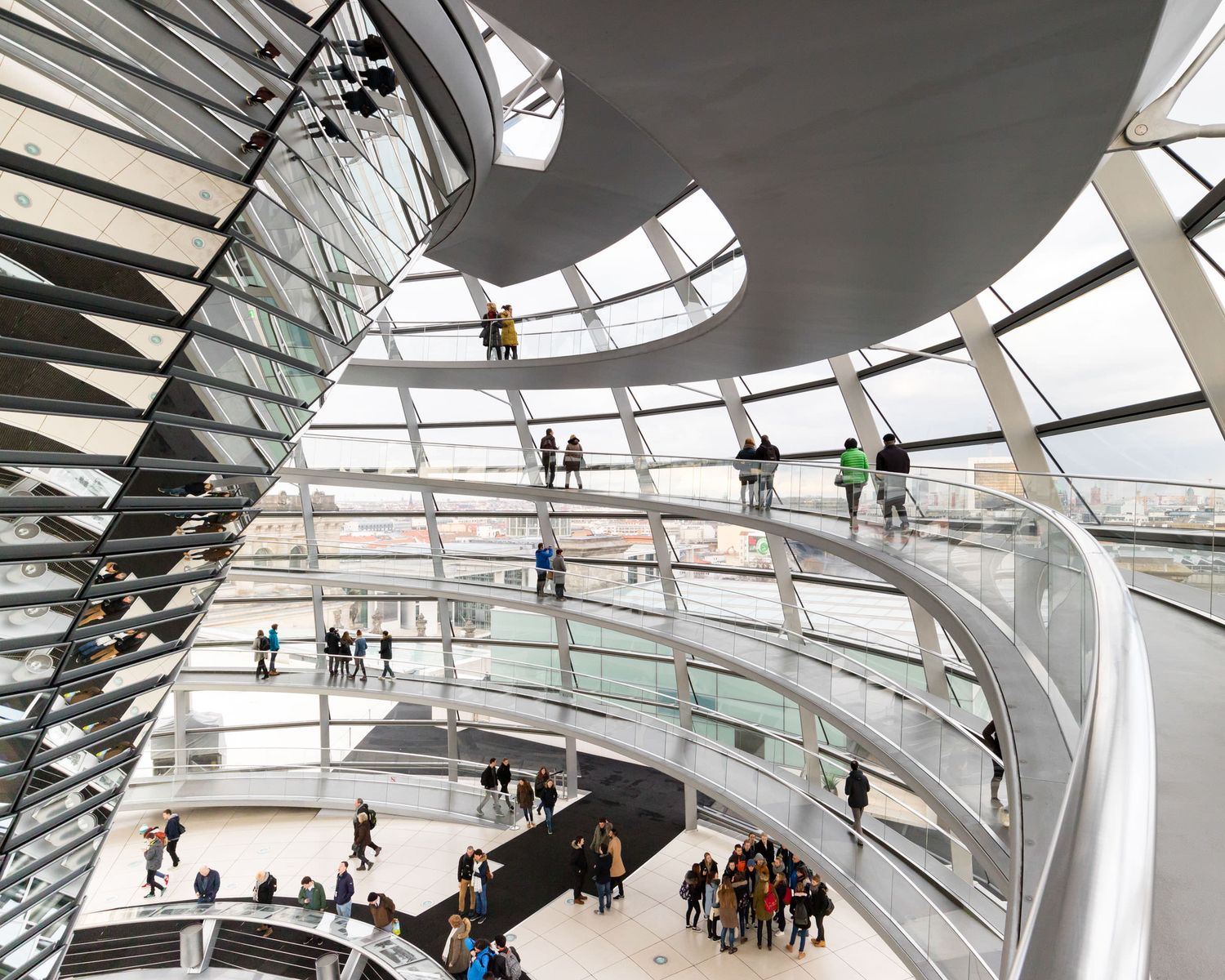 Interior view of the Reichstag glass dome in Berlin with visitors walking along spiral ramps.