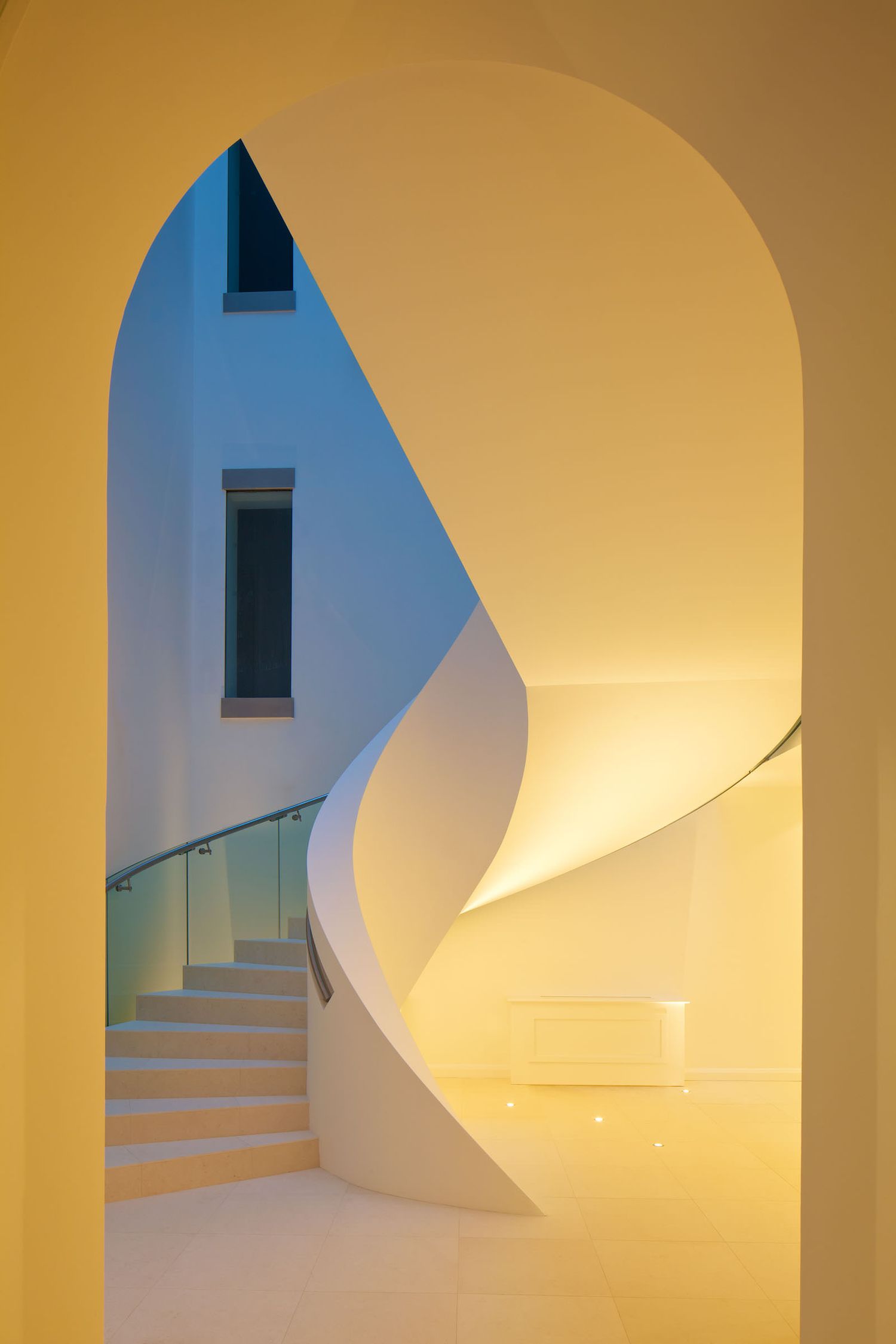 Elegant spiral staircase with warm golden lighting framed by a white arch in modern interior.