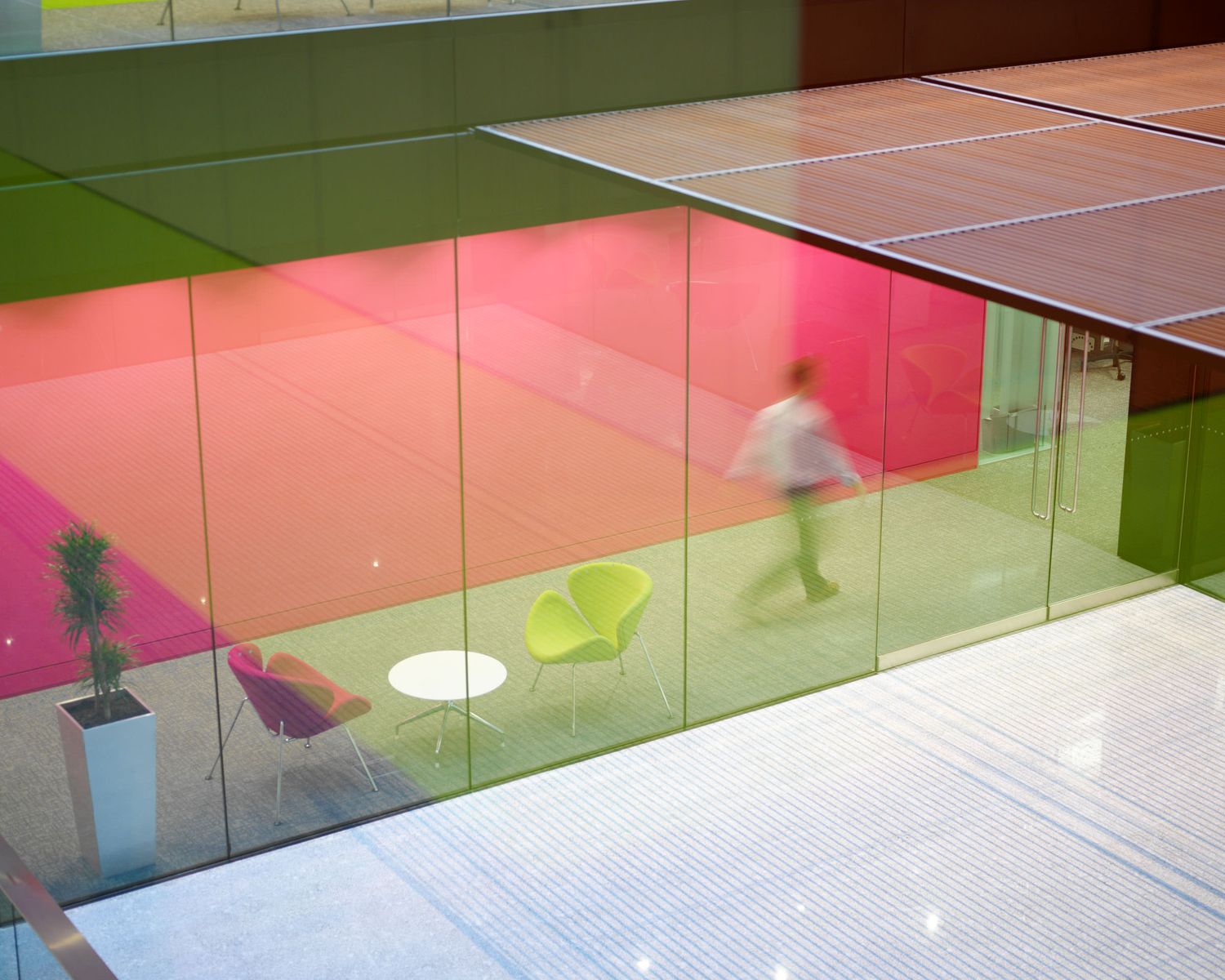 Modern office interior with vibrant pink and green glass partitions and blurred figure walking past.