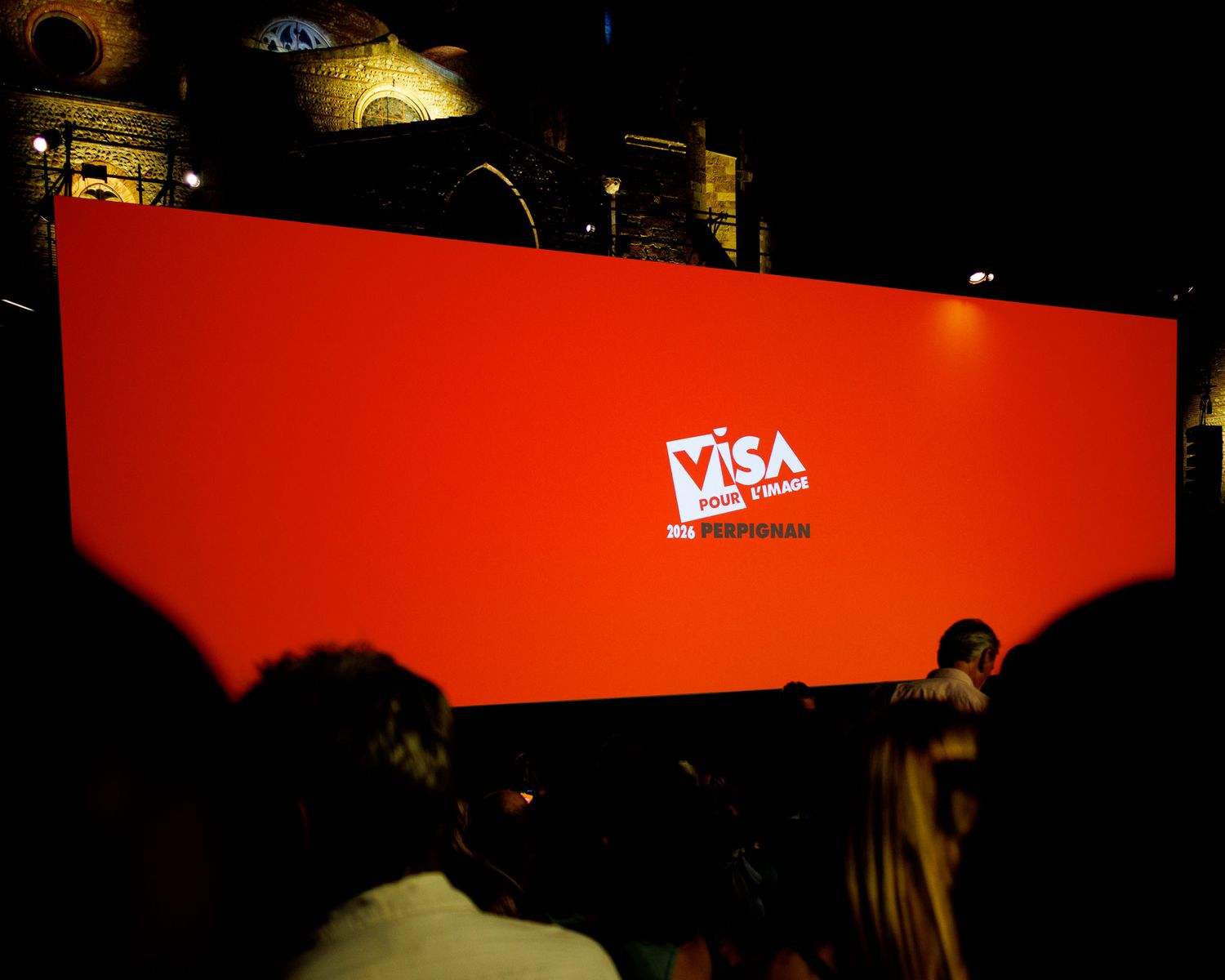 Audience watching a large red Visa pour l Image photography festival screen at an outdoor night event.