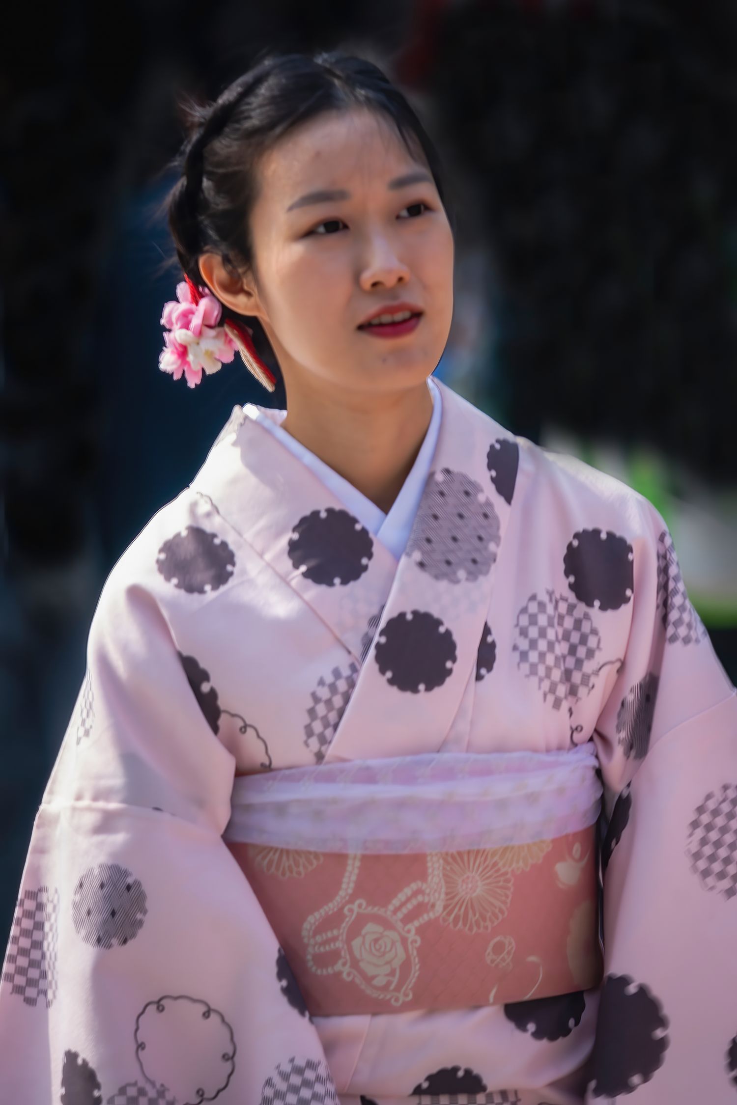 Young Japanese woman in a pink polka dot kimono with floral hair accessory at an outdoor event.