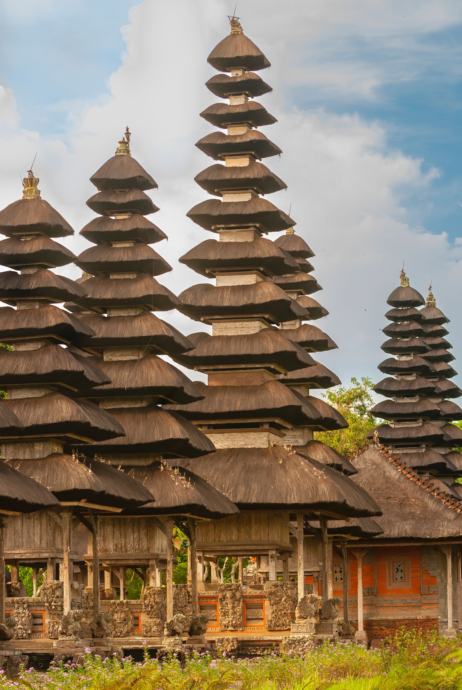 Tall multi-tiered thatched roof pagodas of Pura Taman Ayun royal temple against a blue sky in Bali.