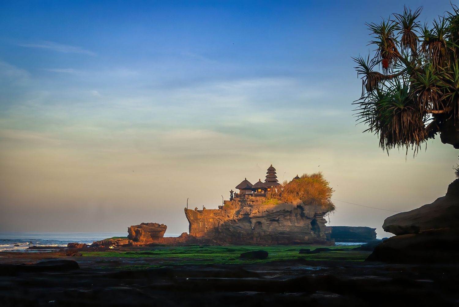 Tanah Lot sea temple sitting on a coastal rock formation bathed in warm sunset light in Bali, Indonesia.