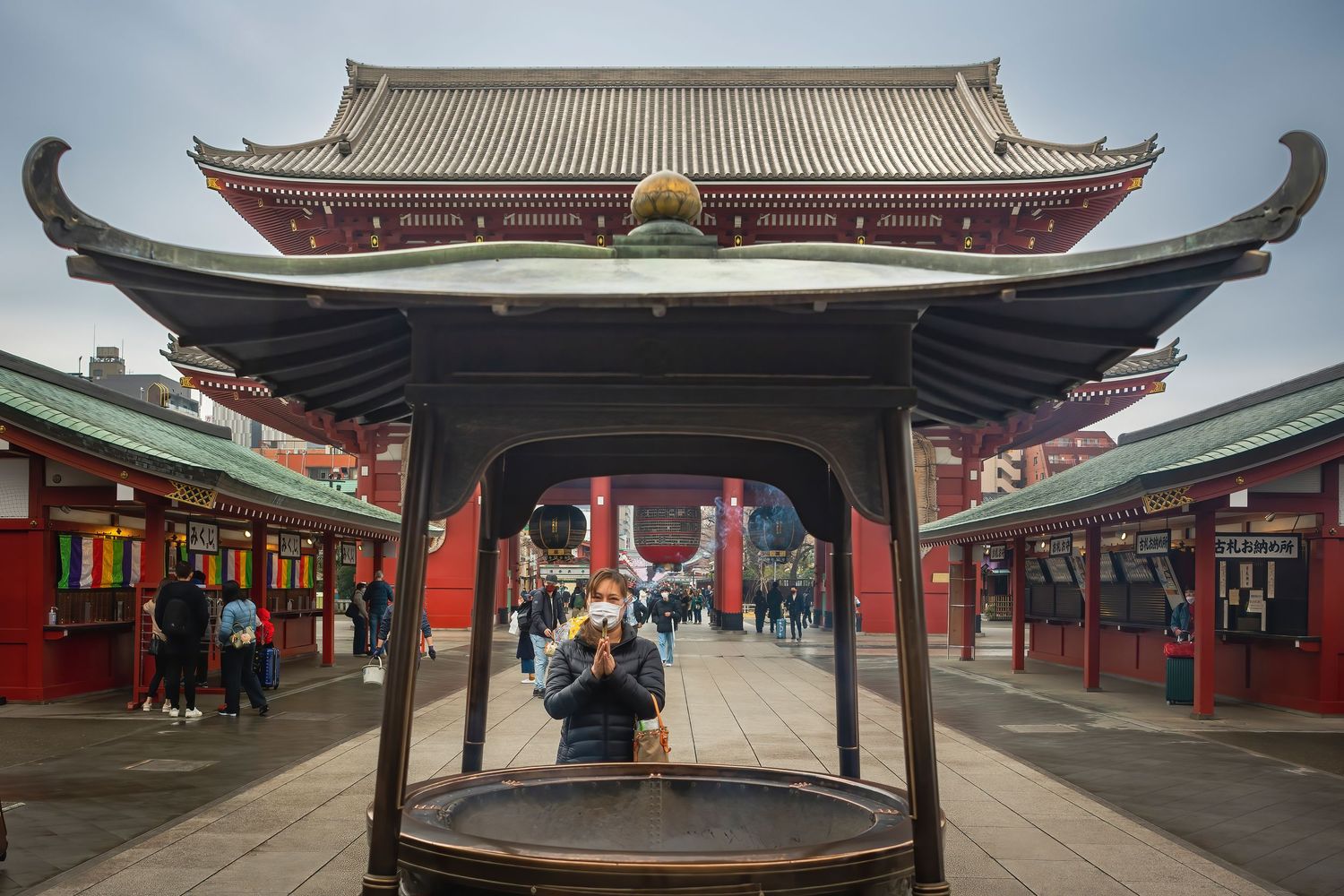 A masked visitor prays at a large incense burner in front of the iconic Senso-ji Temple gate in Tokyo, Japan.