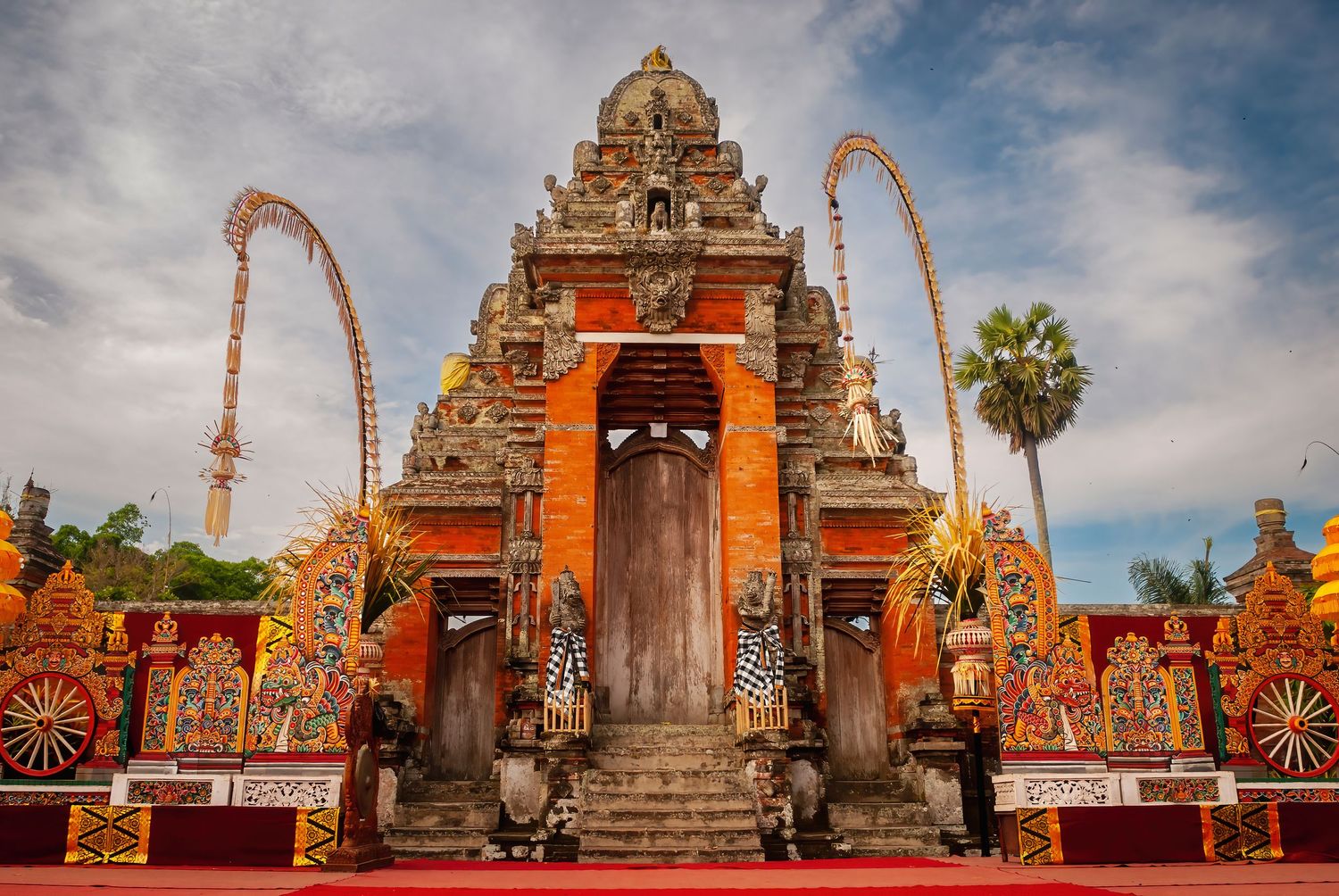 Ornate traditional Balinese Hindu temple gate adorned with colorful orange decorations and intricate carvings.