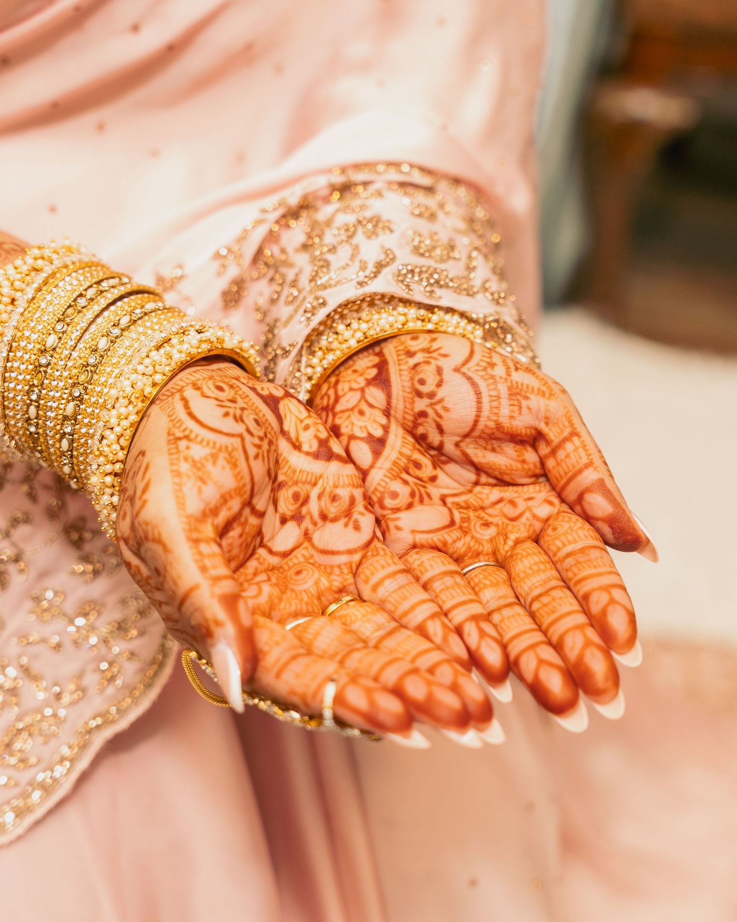 Bride displaying detailed henna mehndi on both palms, adorned with gold bangles.