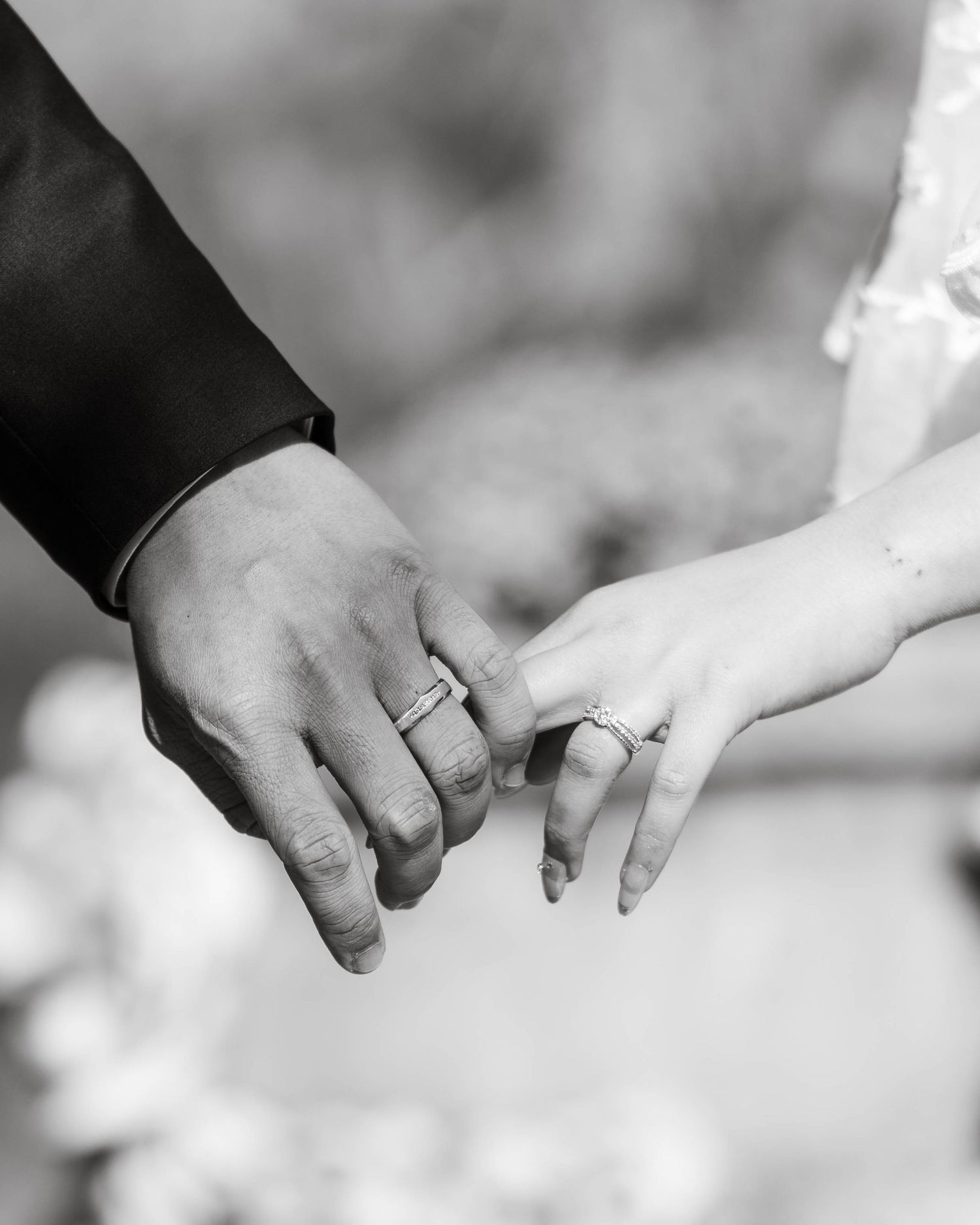 Black and white close-up of bride and groom touching fingers, both wearing wedding bands in elegant wedding attire.