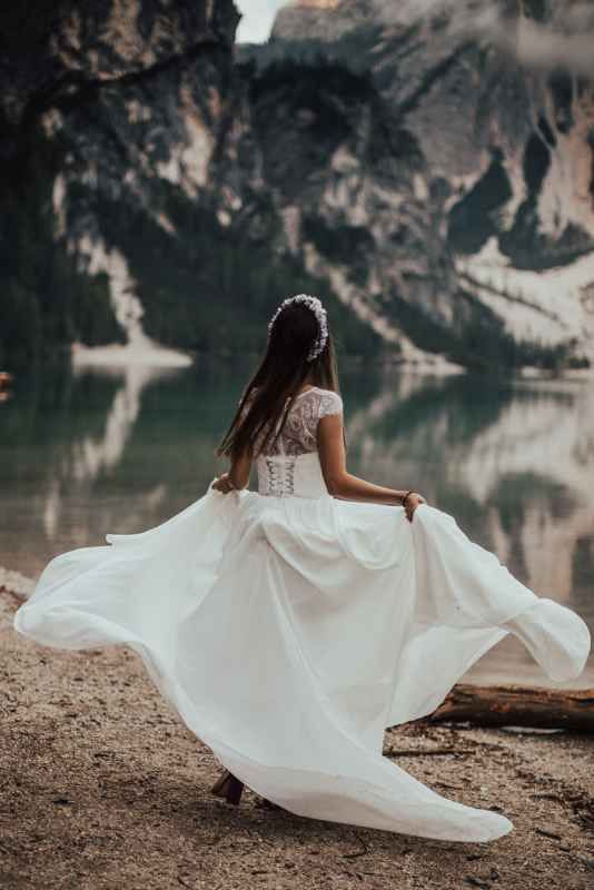 Bride in white lace wedding dress twirling by a mountain lake.
