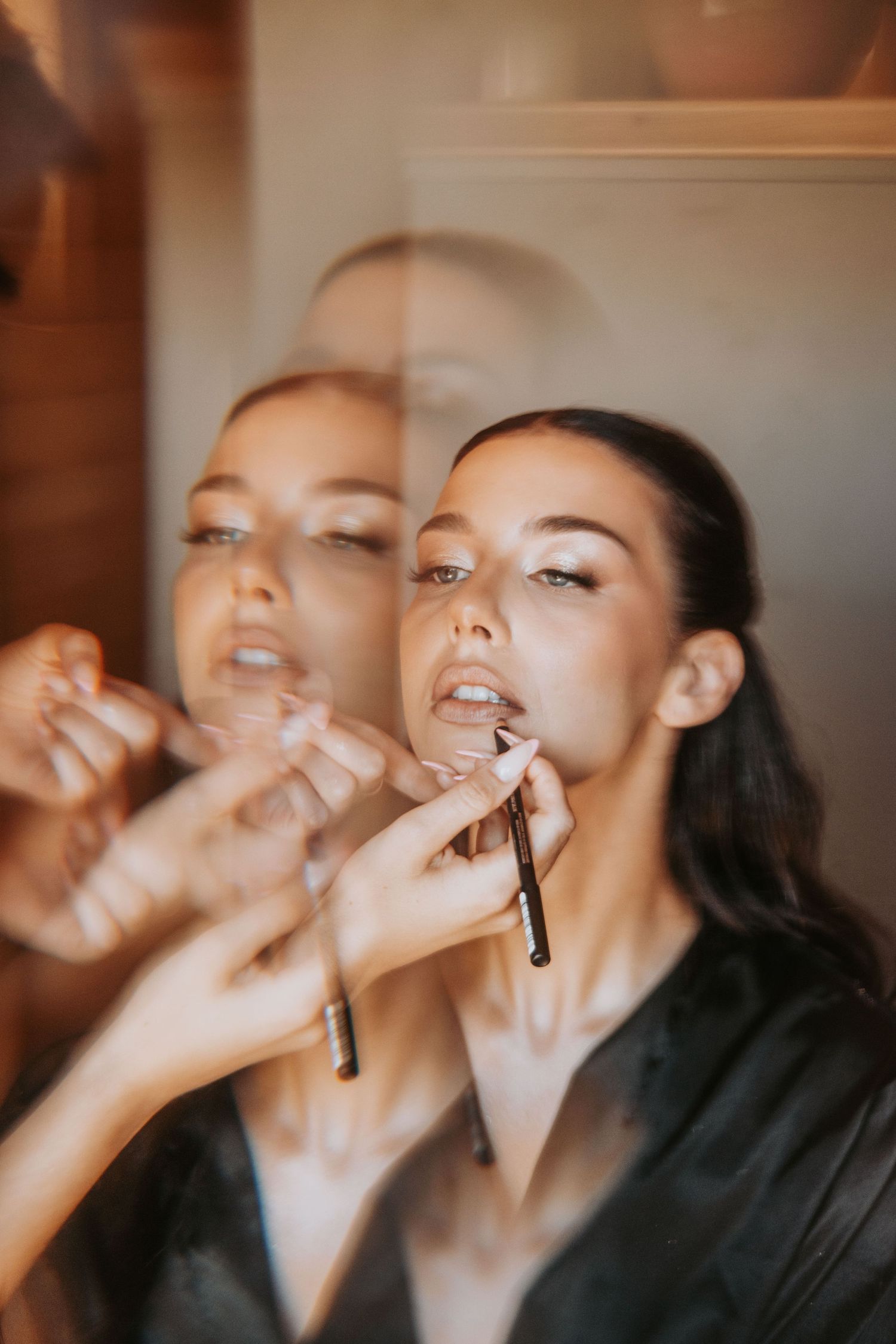 Bride getting lip makeup applied by artist, captured in mirror reflection during wedding preparation.
