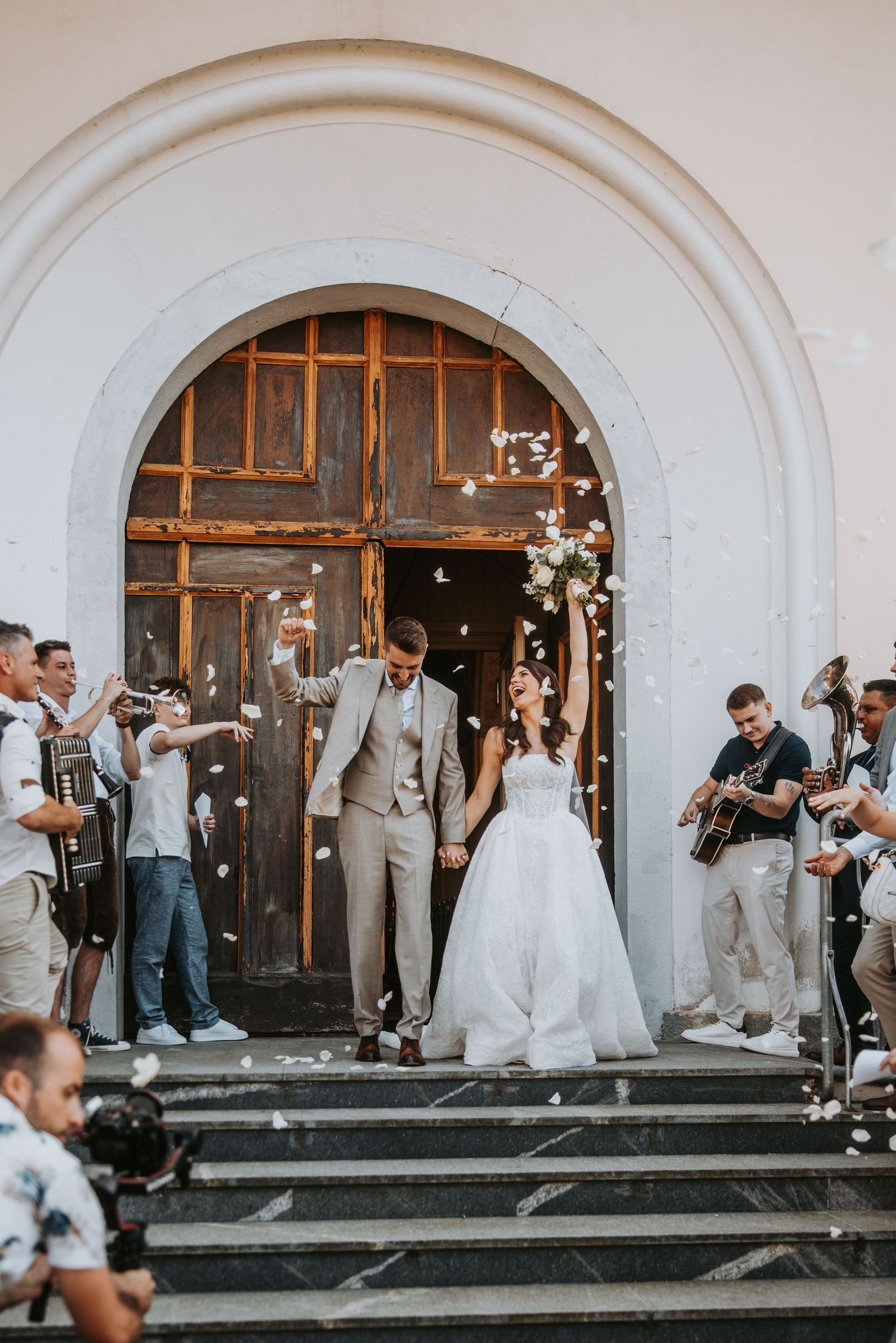 Bride and groom exit church doors as guests toss flower petals in joyful celebration.