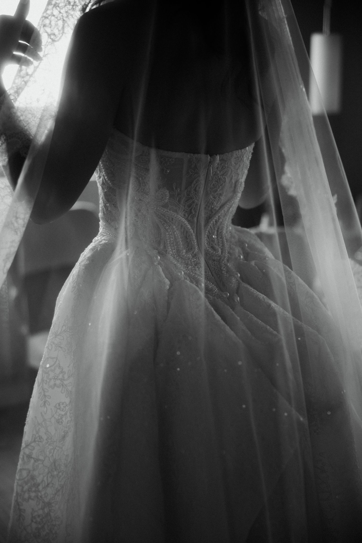 Black and white close-up of a bride's lace wedding dress back with flowing veil.