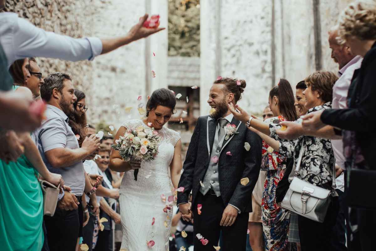 Joyful newlyweds walking through a confetti shower surrounded by cheering guests after their ceremony.