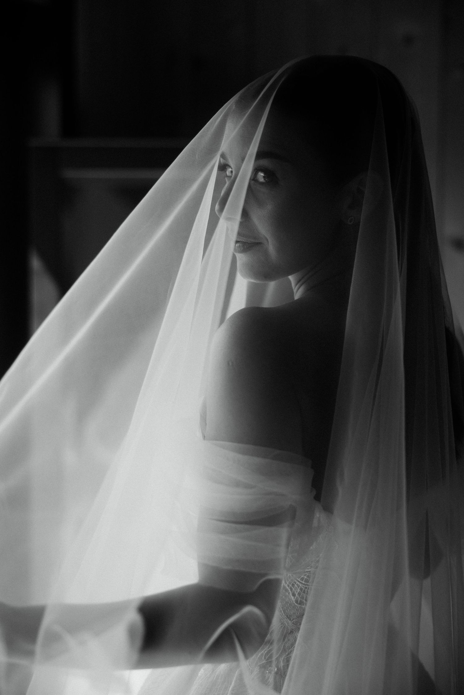Elegant black and white portrait of a bride draped in a flowing veil with soft lighting.