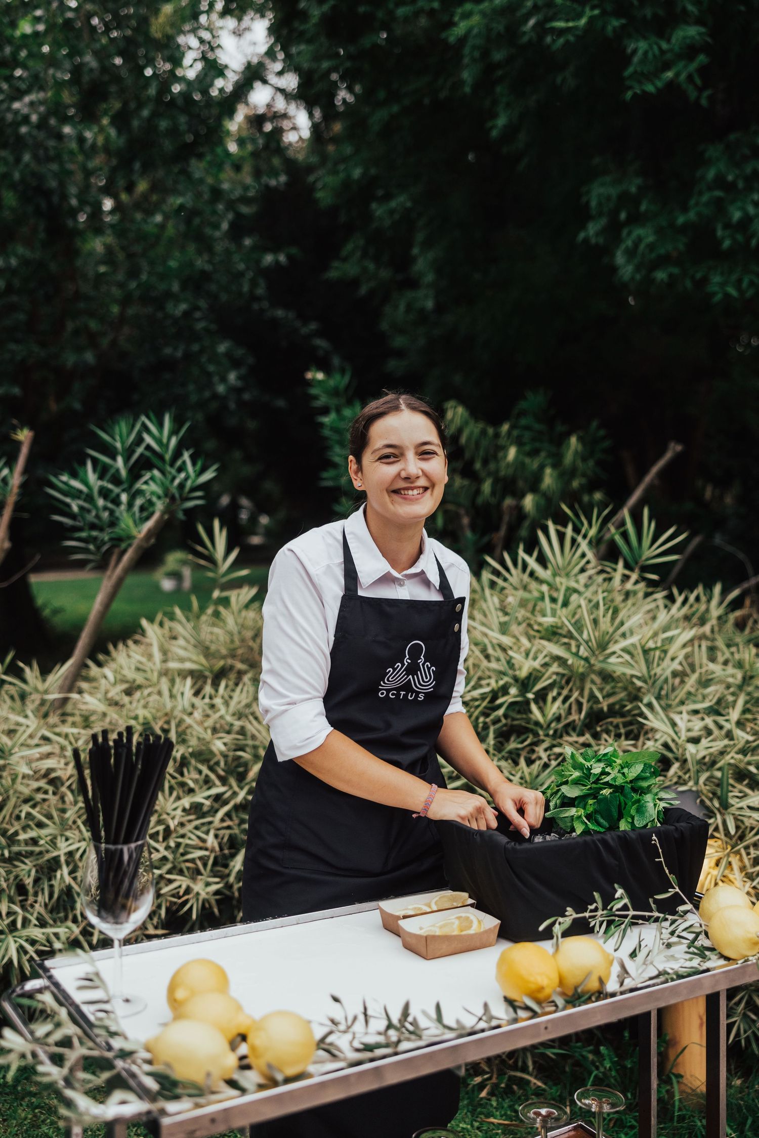 Smiling female catering staff in black apron preparing food at outdoor wedding.