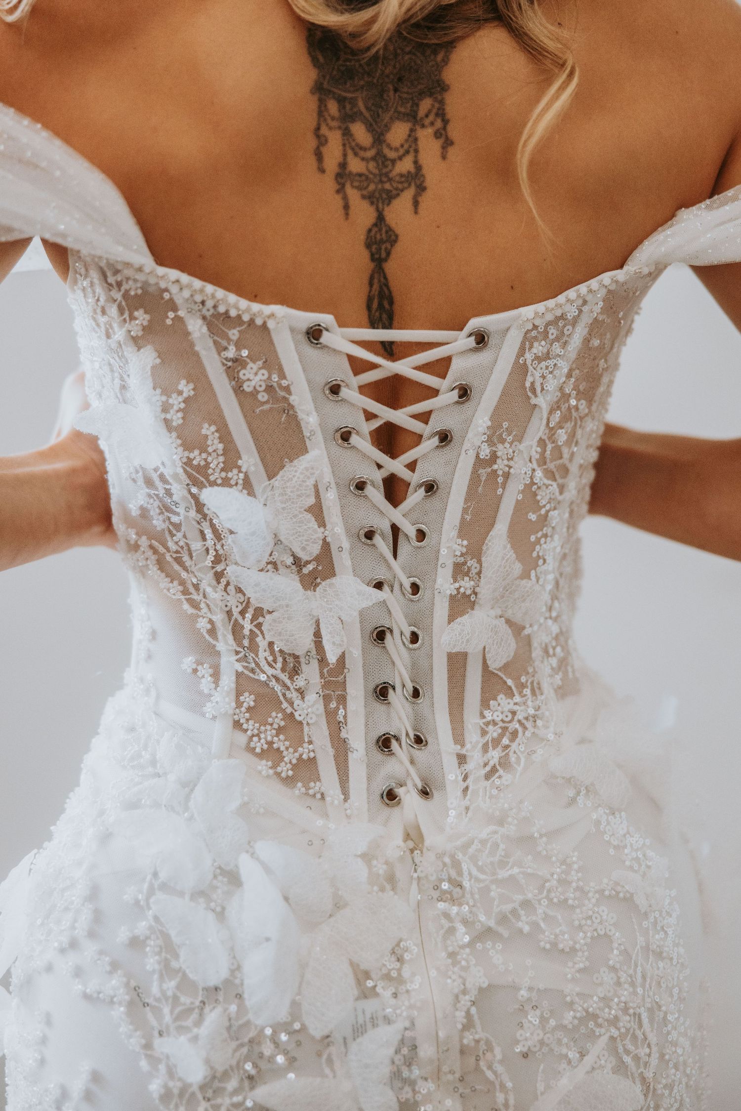 Close-up back view of intricate lace corset wedding dress with butterfly details and back tattoo.
