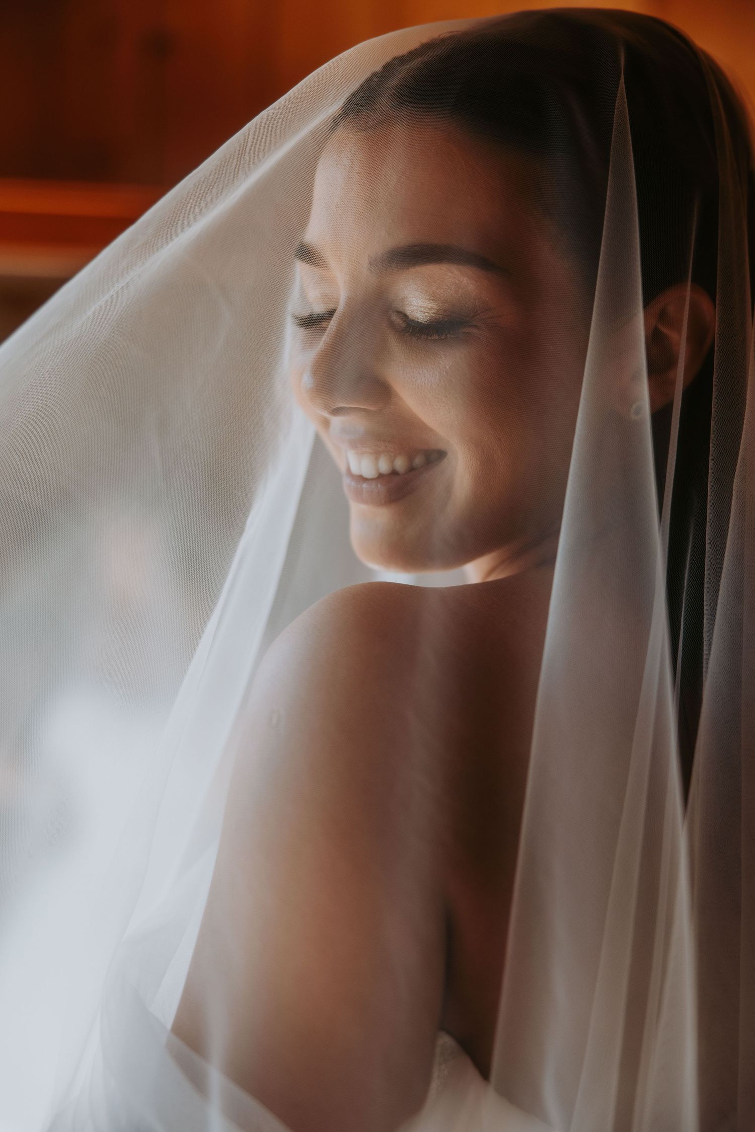 Radiant bride smiling softly under a flowing white wedding veil in warm natural light.