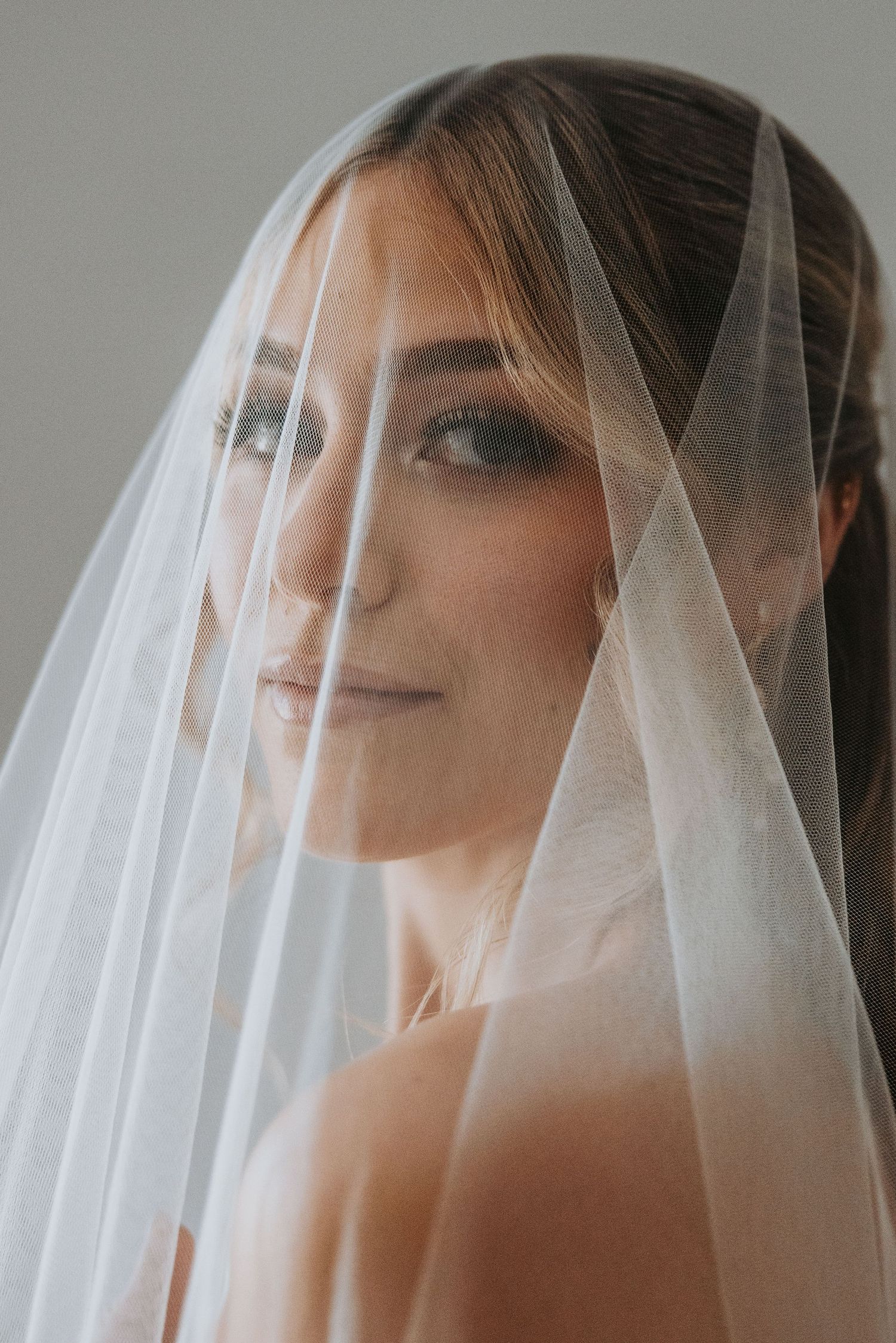 Intimate portrait of bride with smoky eye makeup gazing through a delicate white wedding veil.
