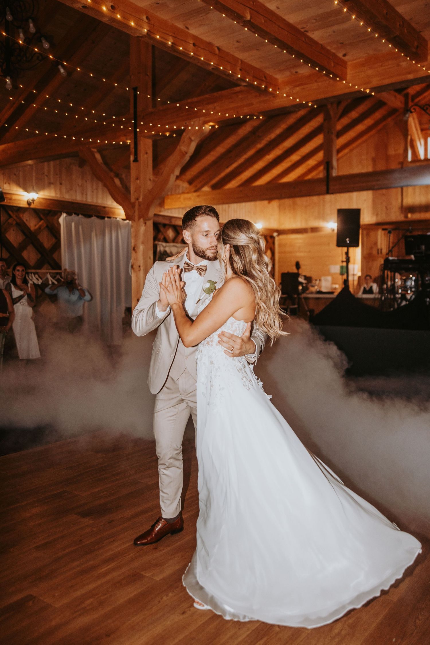 Bride and groom share their first dance in a rustic barn venue with string lights and fog effects.