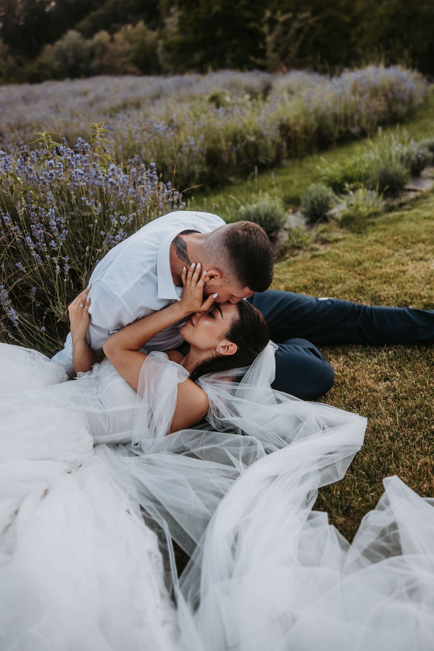 Bride and groom sharing a romantic kiss while lying together in a lush lavender field.