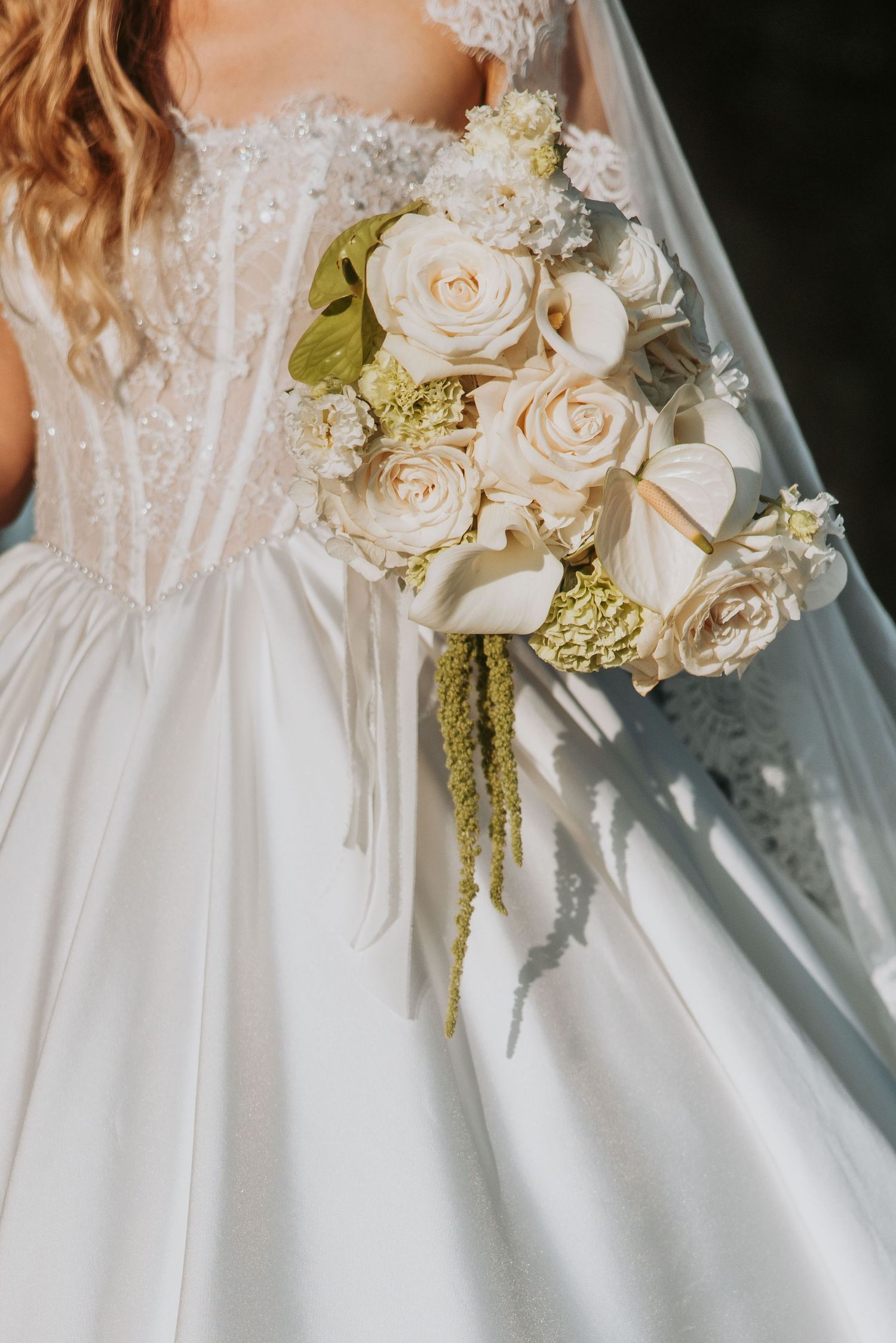 Close-up of bride holding cascading white rose bouquet against beaded lace wedding gown bodice.