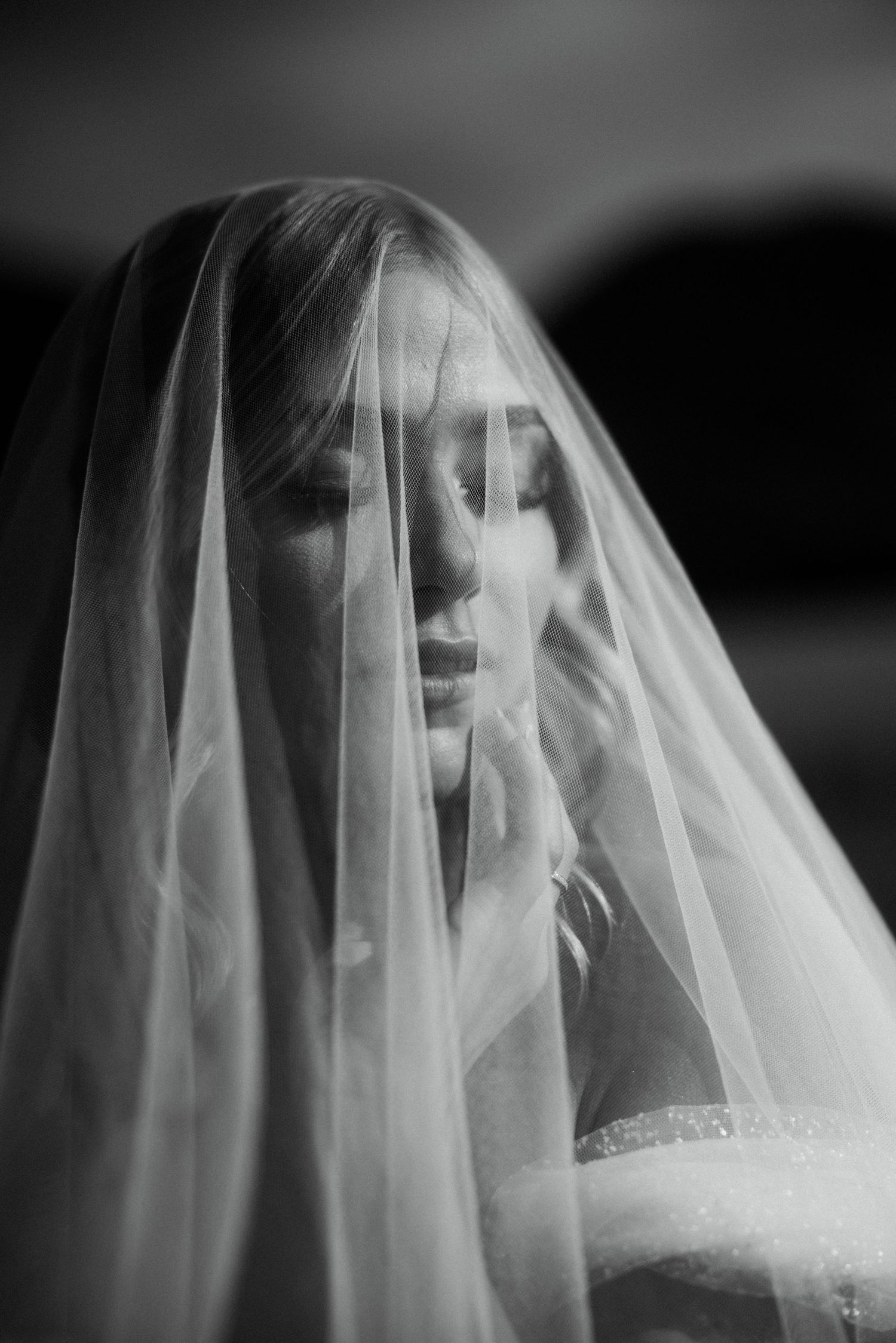Black and white portrait of bride covered by sheer wedding veil.
