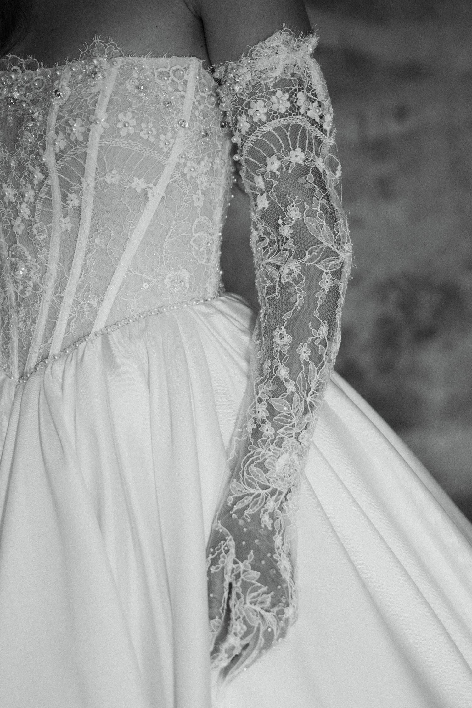 Black and white close-up of a bride in a lace corset wedding gown wearing elegant long floral lace gloves.