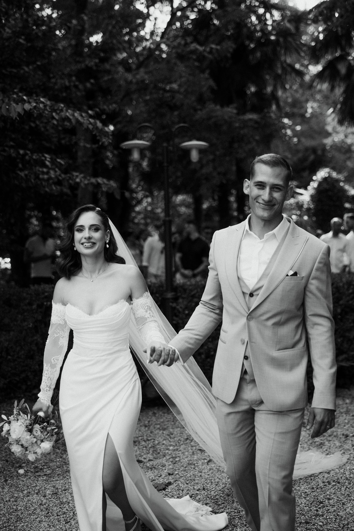 Bride and groom walk hand in hand smiling in black and white wedding portrait outdoors.