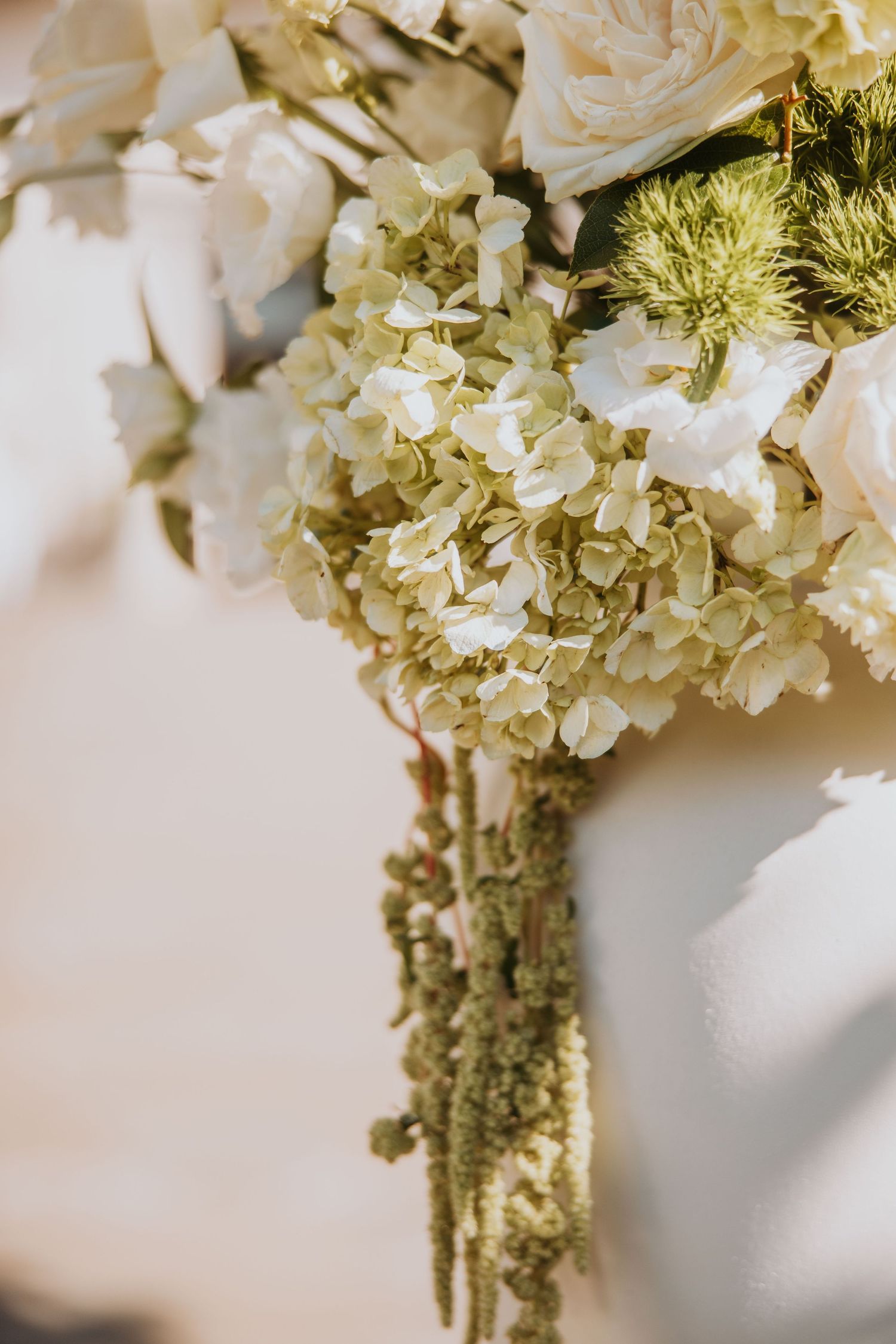 Close-up of elegant wedding bouquet featuring white hydrangeas, roses, and trailing green amaranthus.