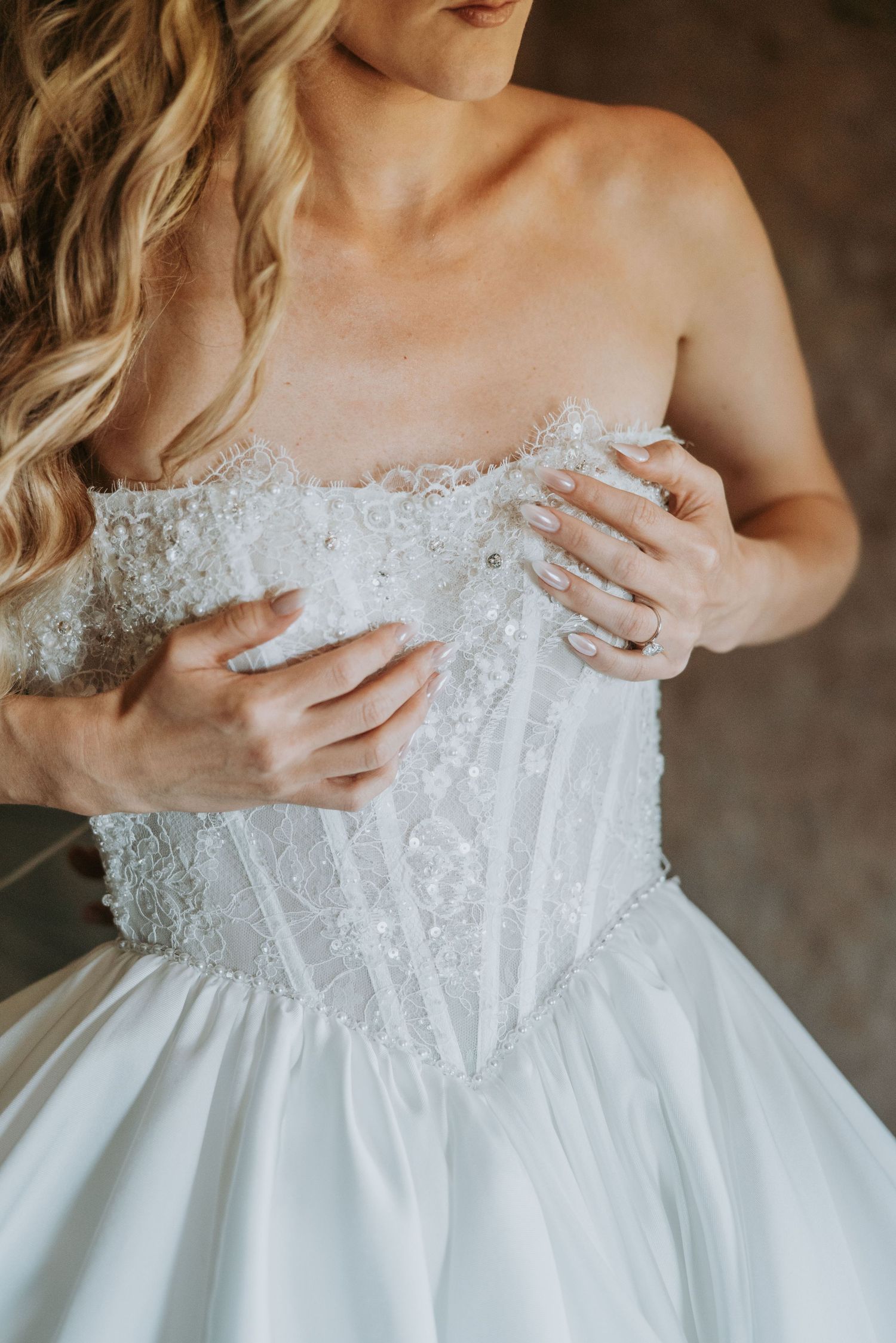Bride adjusting her strapless lace corset wedding dress bodice with manicured hands.