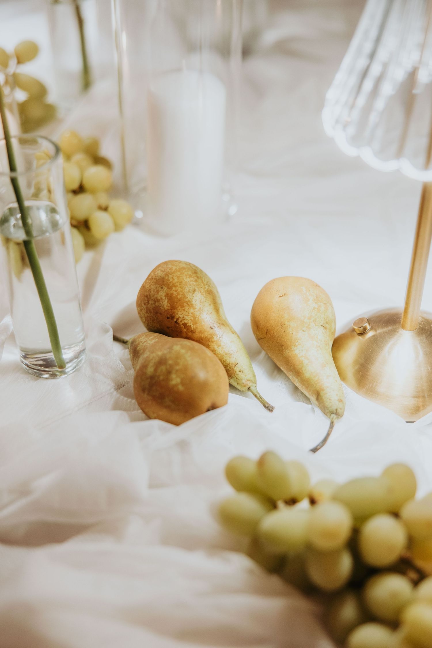 Wedding table decor with golden pears, green grapes, candles, and white fabric centerpiece.