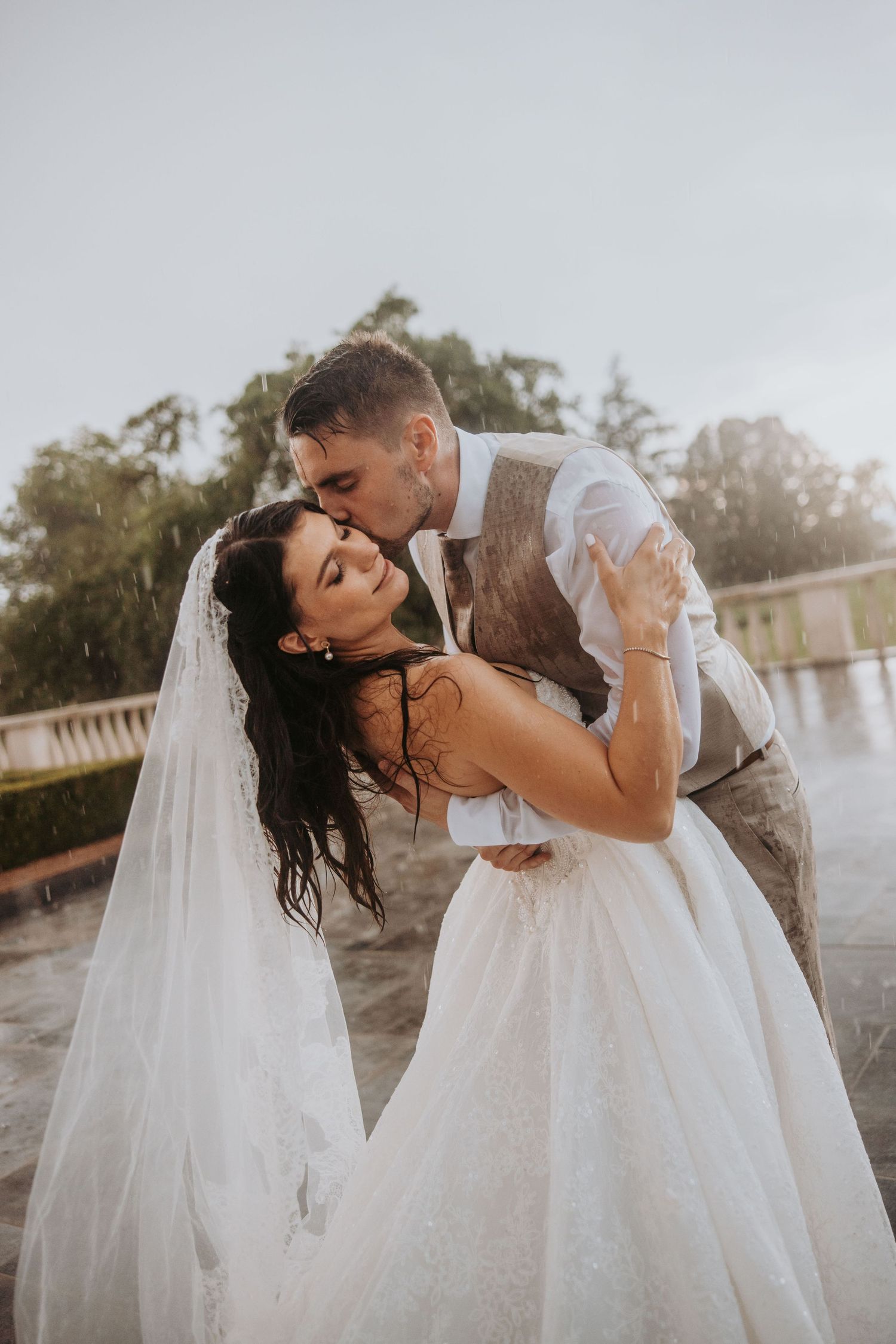 Bride and groom share passionate kiss in the rain during outdoor wedding portraits.