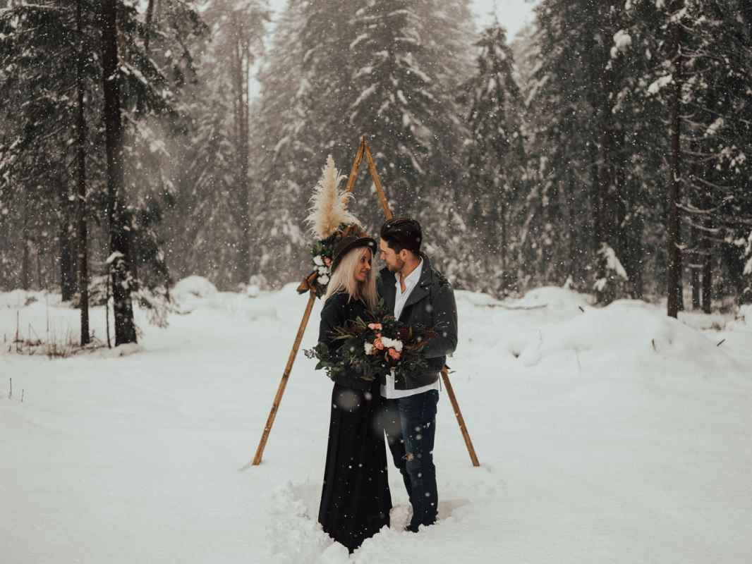 Couple exchanging vows under a wooden arch in a snowy winter forest during a blizzard.