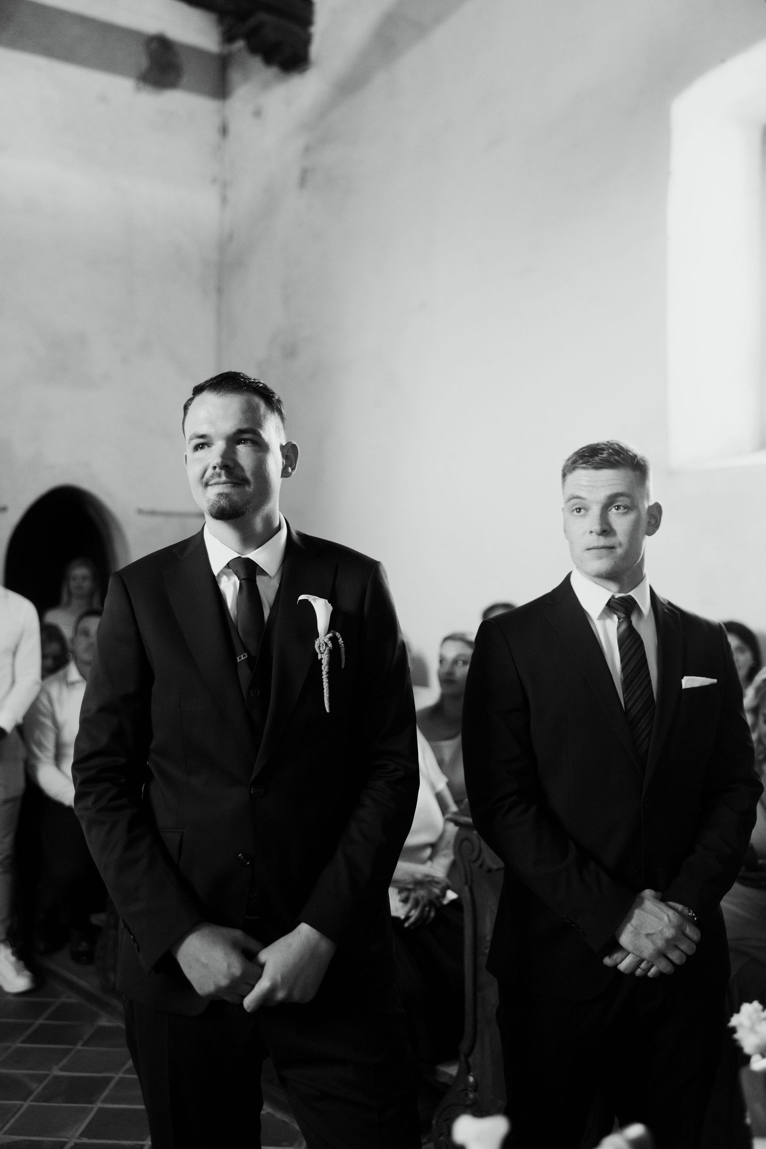 Two groomsmen in black suits stand at the altar awaiting the bride during a church wedding ceremony.