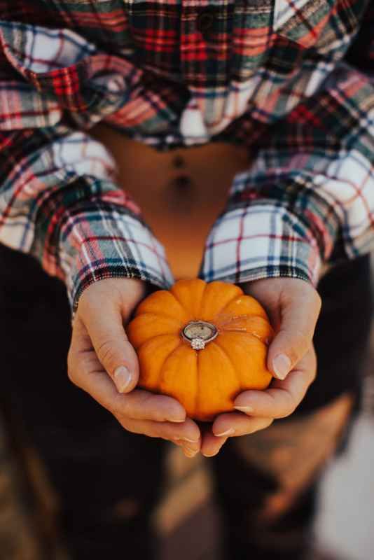 Person in plaid shirt holding a small orange pumpkin with a ring on top in cupped hands.