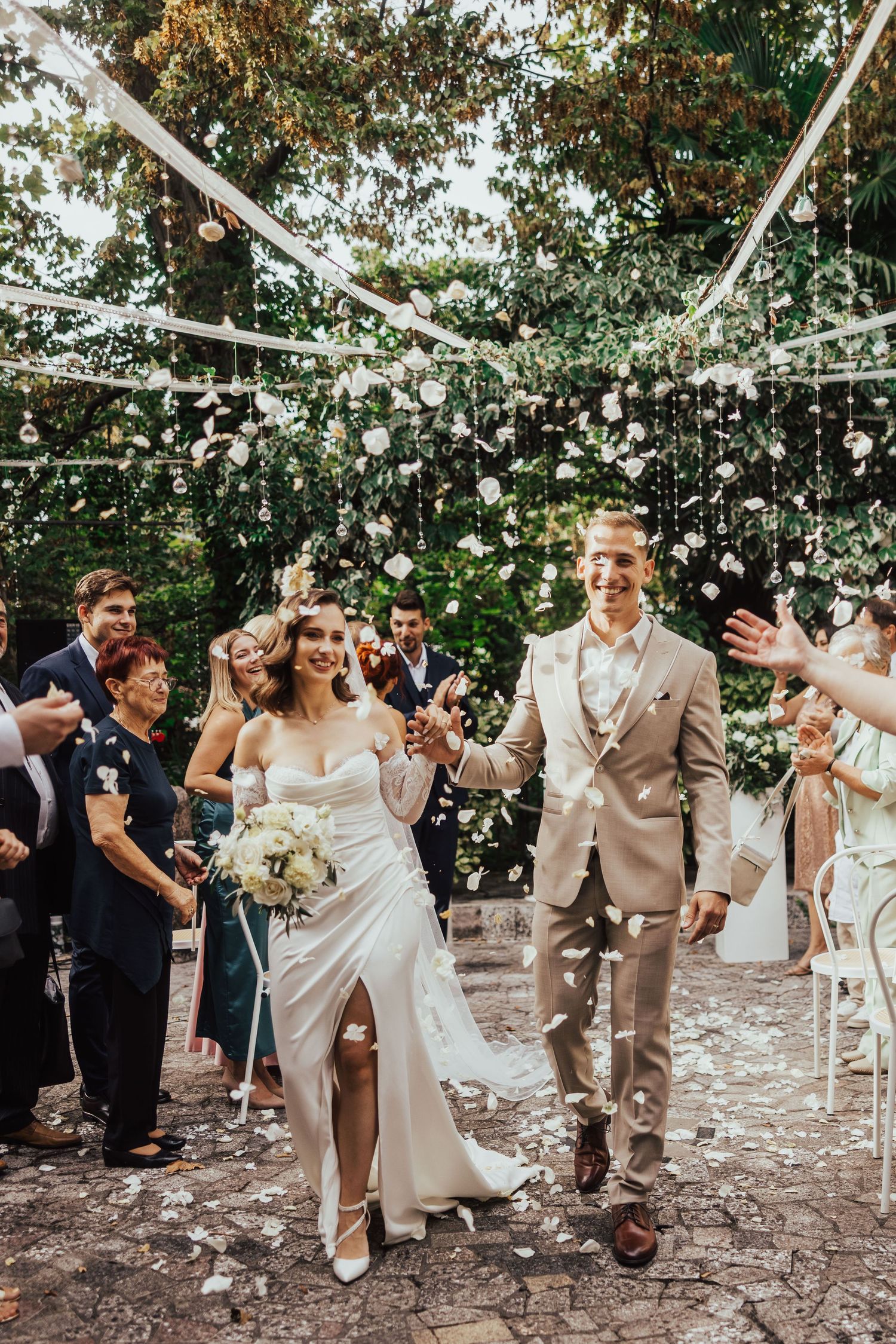 Joyful newlyweds walking down the aisle as guests shower them with white confetti outdoors.