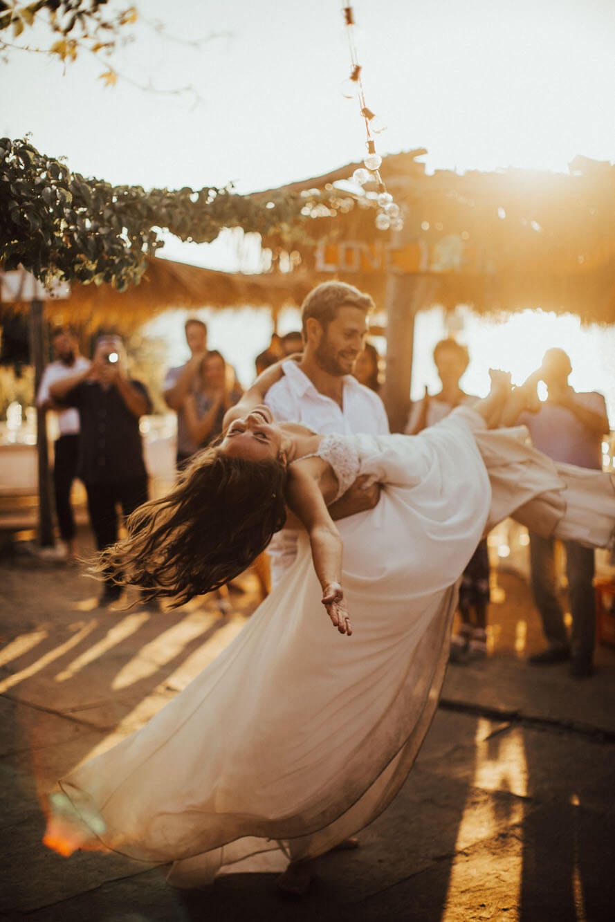 Couple sharing first dance at golden hour outdoor wedding reception with string lights and guests.
