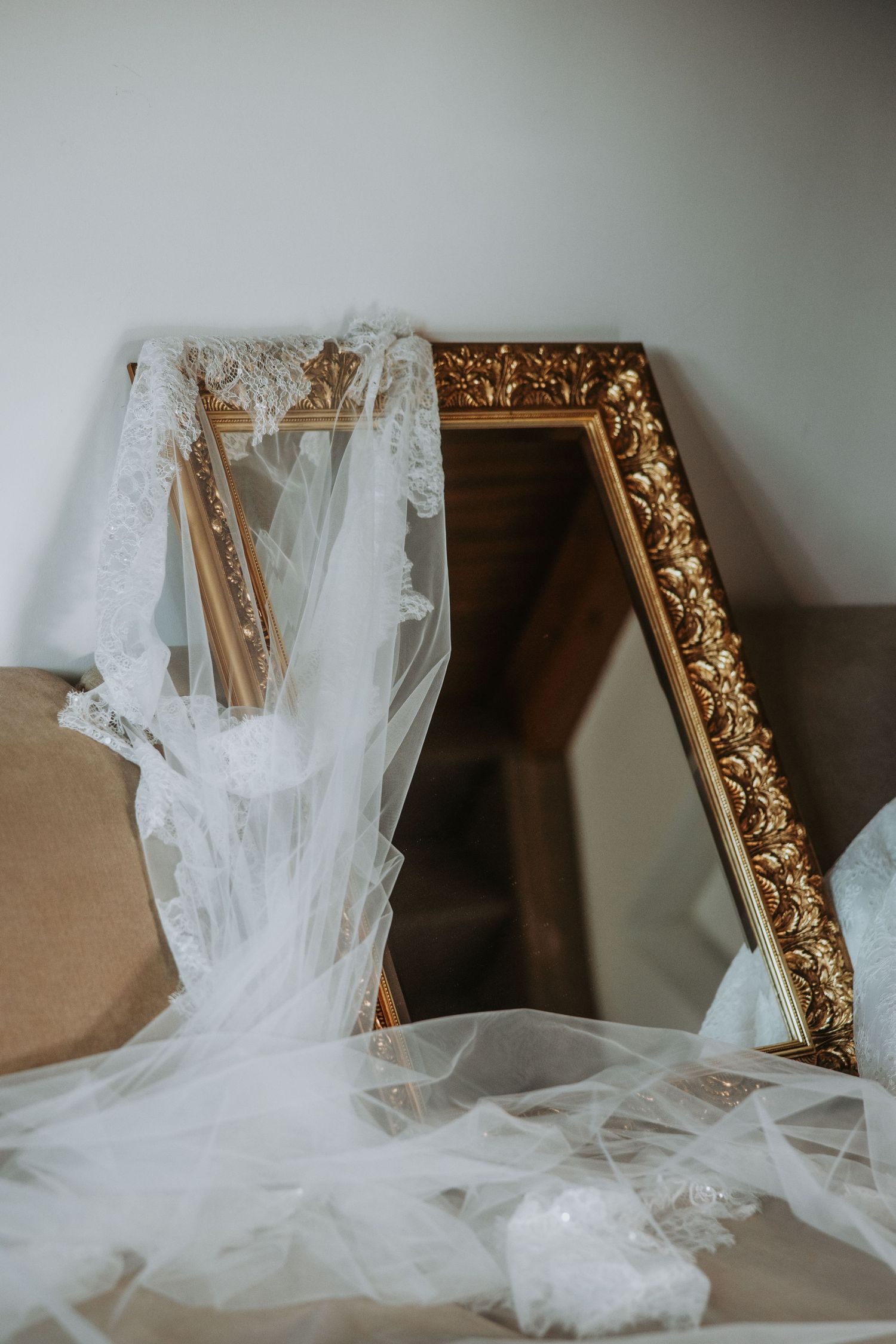 Elegant bridal veil with lace trim draped over a ornate gold-framed mirror, wedding preparation details.