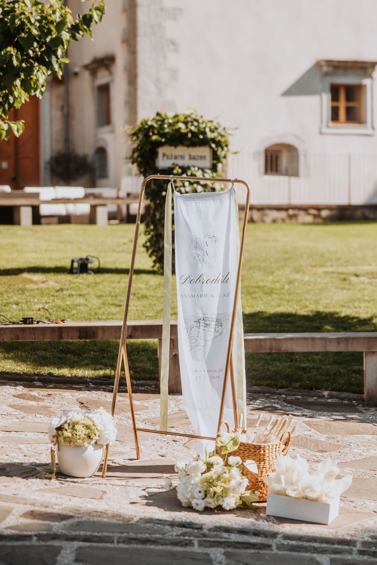 Gold rack with personalized wedding welcome banner and white floral arrangements outdoors.