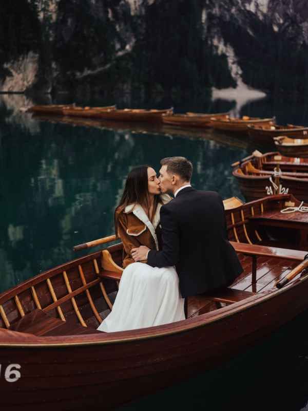 Wedding couple sharing a kiss in a wooden rowboat on a serene turquoise mountain lake.