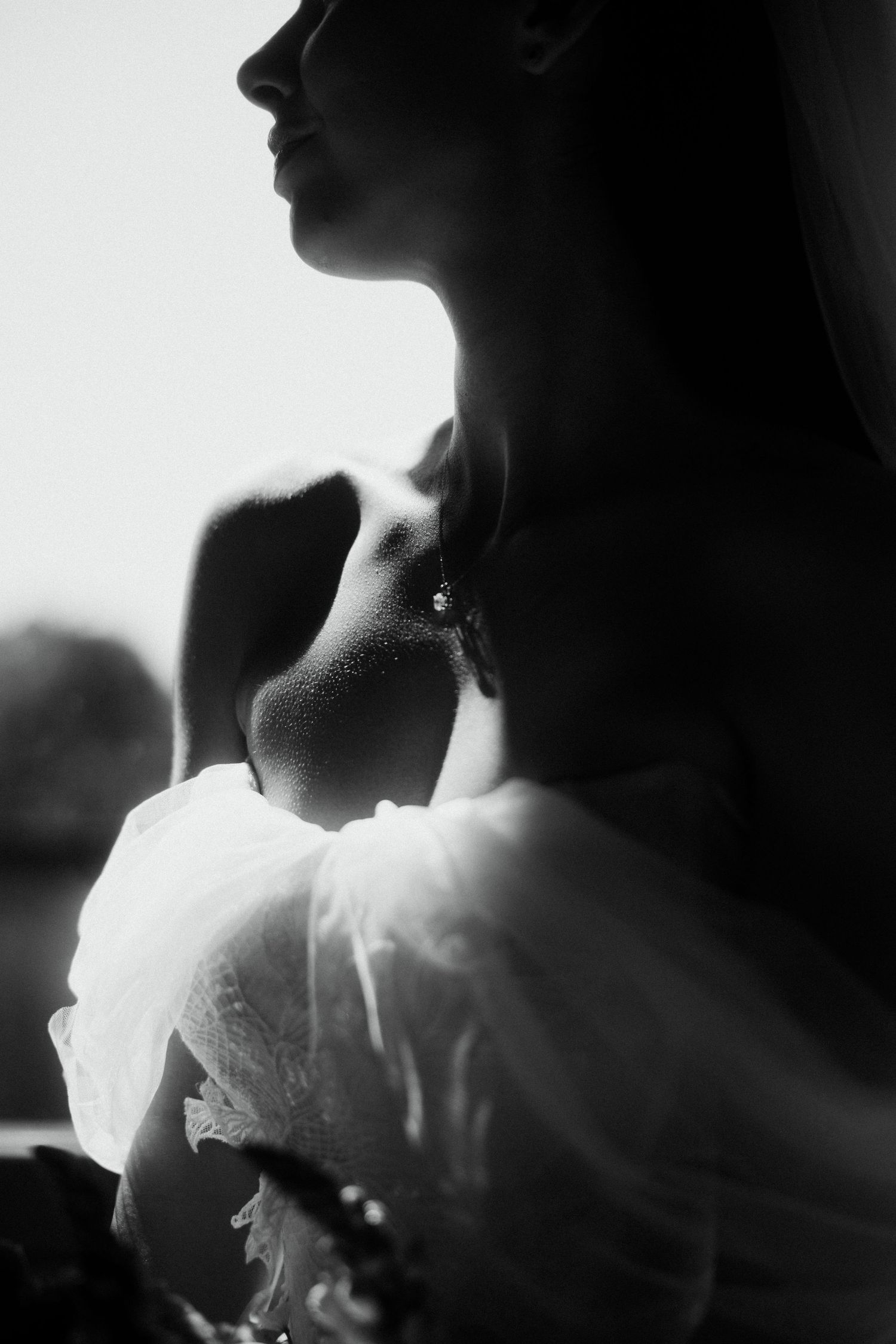 Black and white portrait of a bride wearing a drop earring and white lace dress, bathed in soft light.