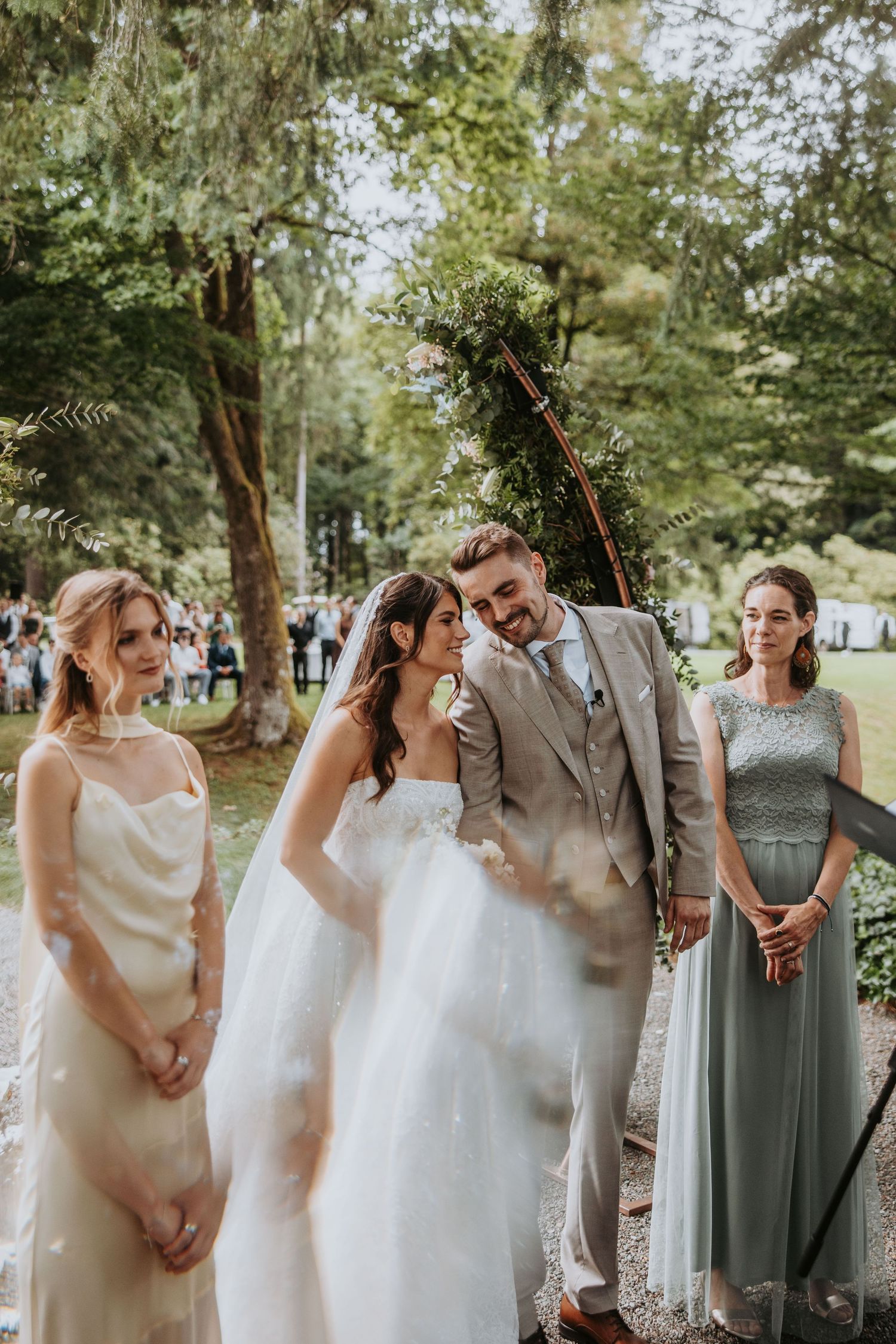 Bride and groom share a joyful moment with bridesmaids during outdoor wedding ceremony in park.