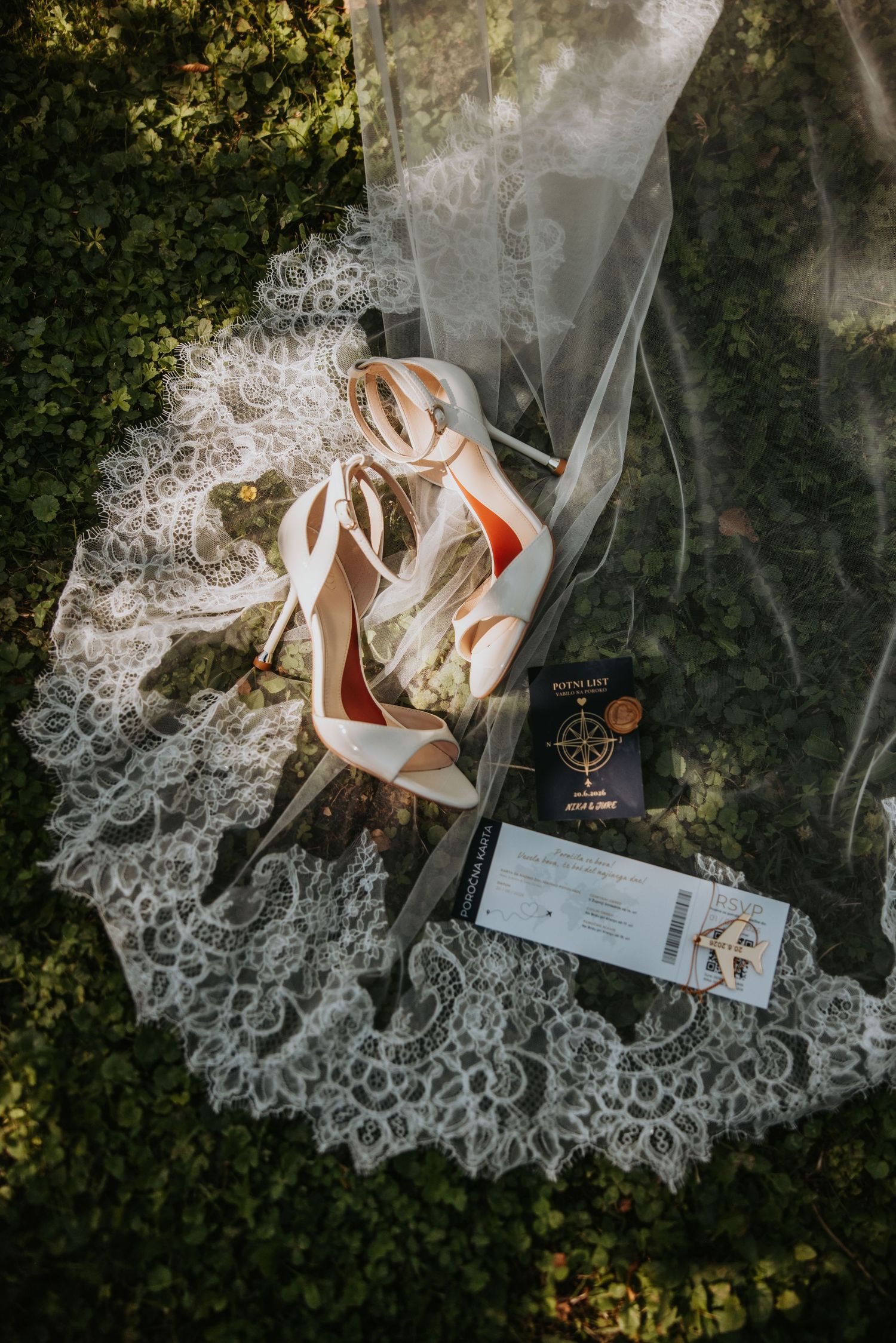 Bridal flat lay with white lace veil, strappy heels, passport, and boarding pass on green grass.