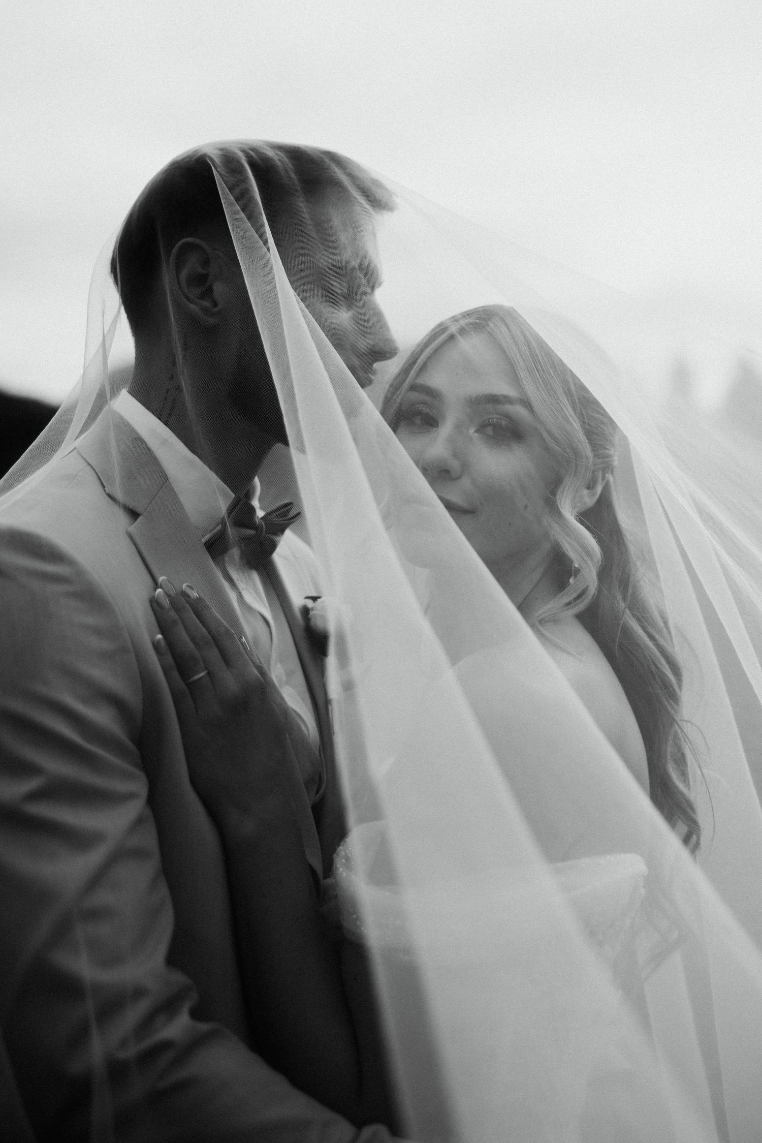Romantic black and white portrait of bride and groom sharing intimate moment beneath flowing wedding veil.