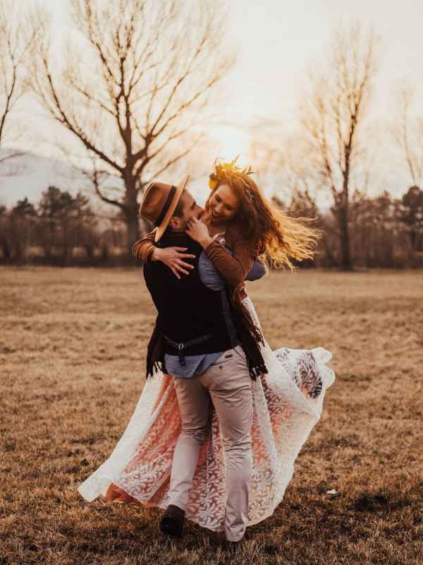 Joyful couple spinning and embracing at golden sunset in an open autumn field.