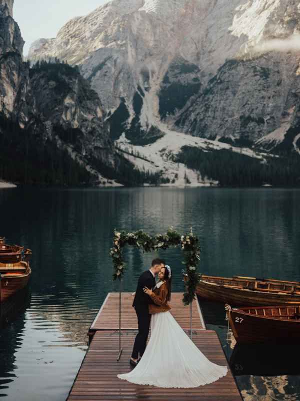 Wedding couple kissing on a dock at Lake Braies with stunning alpine mountains and wooden boats.