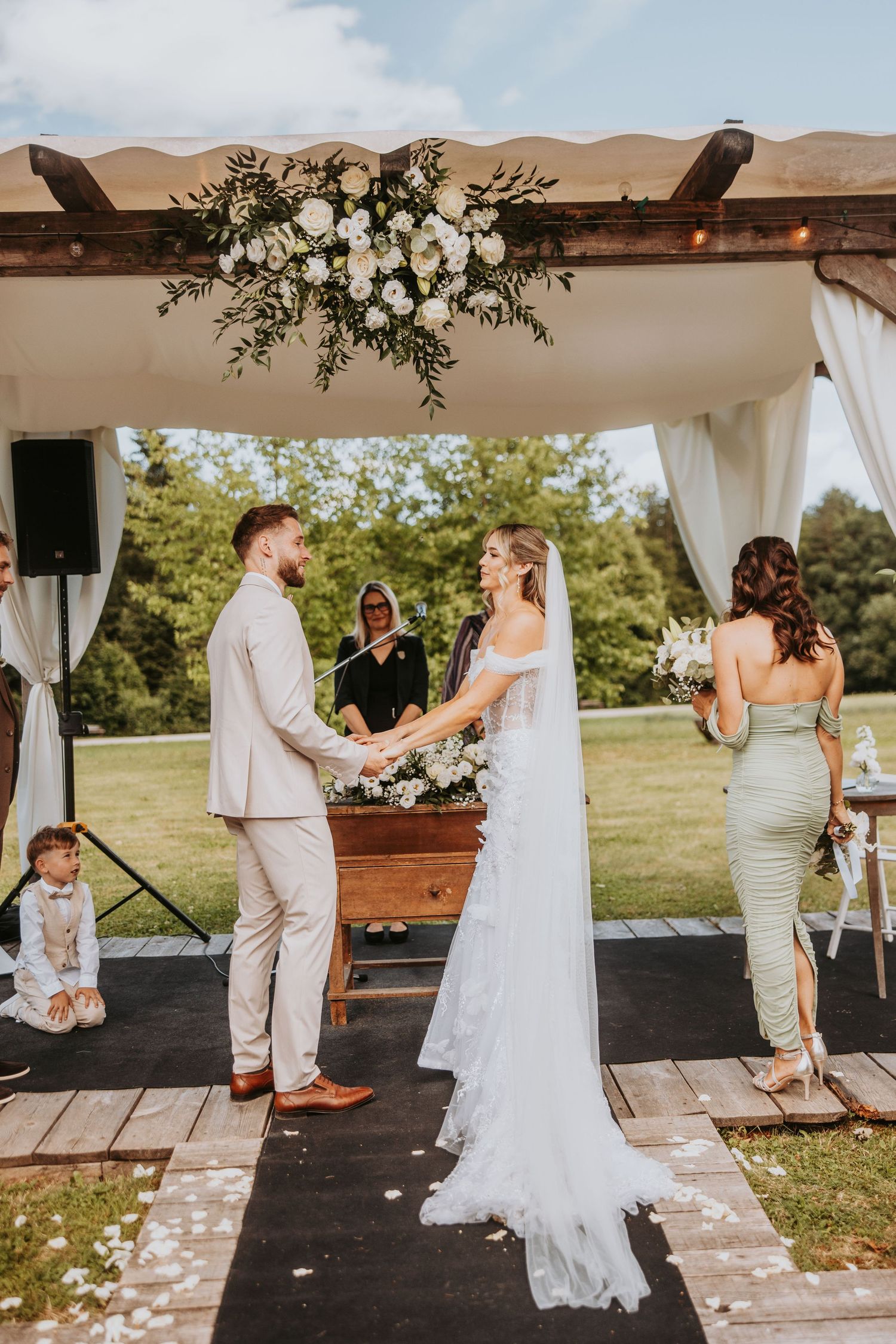 Bride and groom exchanging vows at outdoor wedding altar adorned with white roses and greenery.