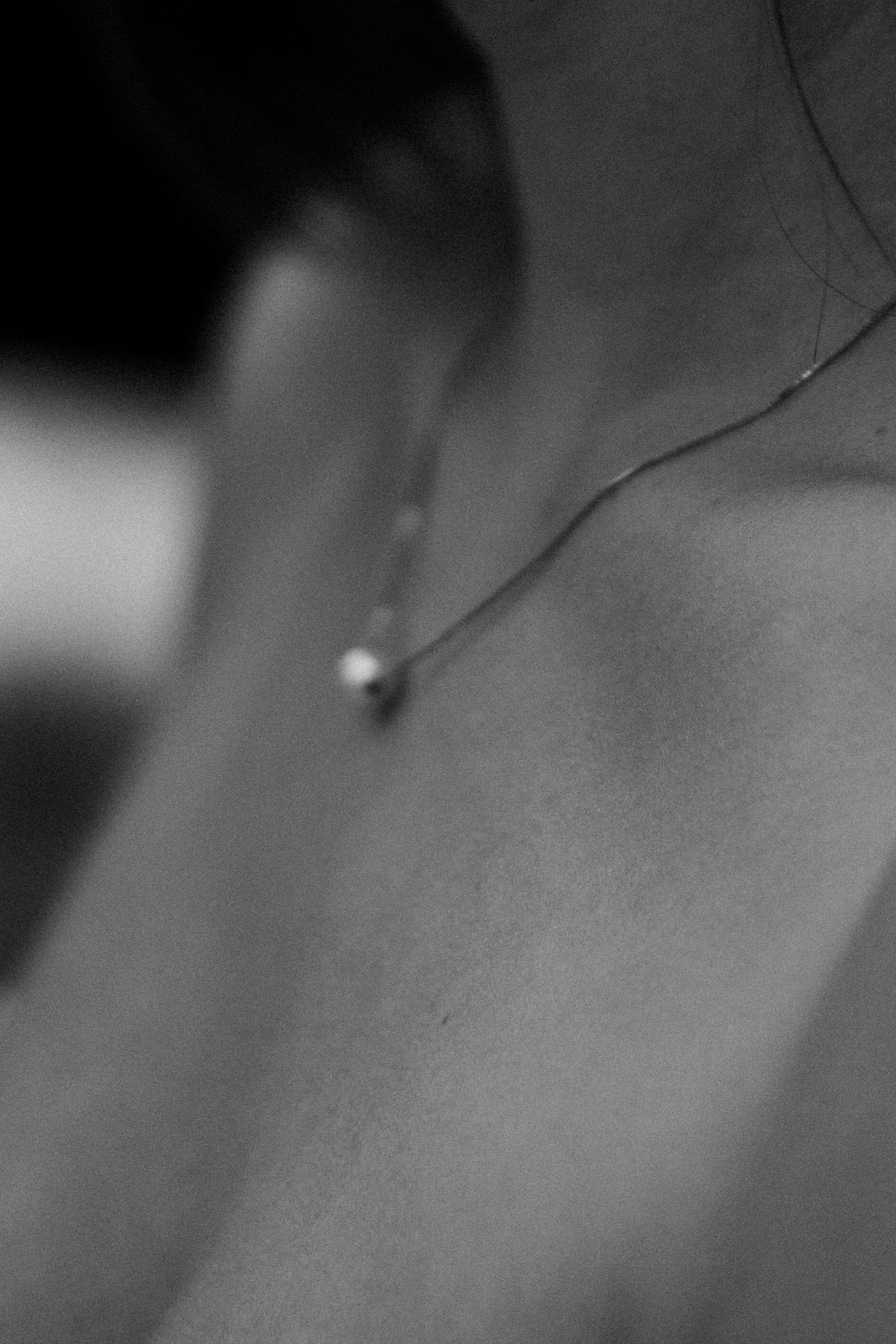 Close-up black and white photo of a delicate diamond pendant necklace resting on a brides collarbone.