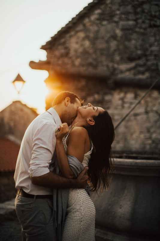 Romantic couple embracing at golden sunset near ancient stone building, man kissing woman who laughs joyfully.