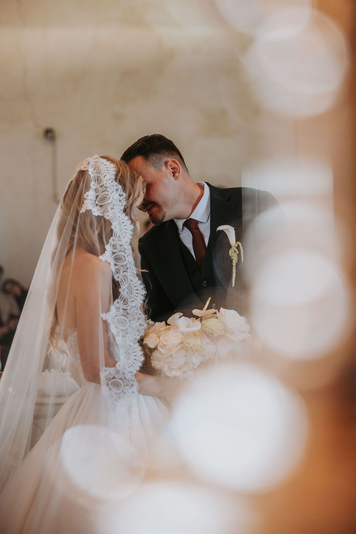 Bride and groom sharing an intimate moment at the altar during wedding ceremony, bride wearing lace cathedral veil.