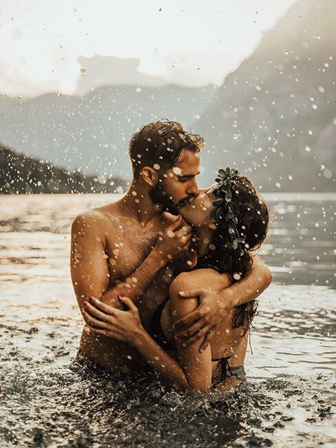 Couple kissing passionately in a mountain lake with water splashing around them at golden hour.
